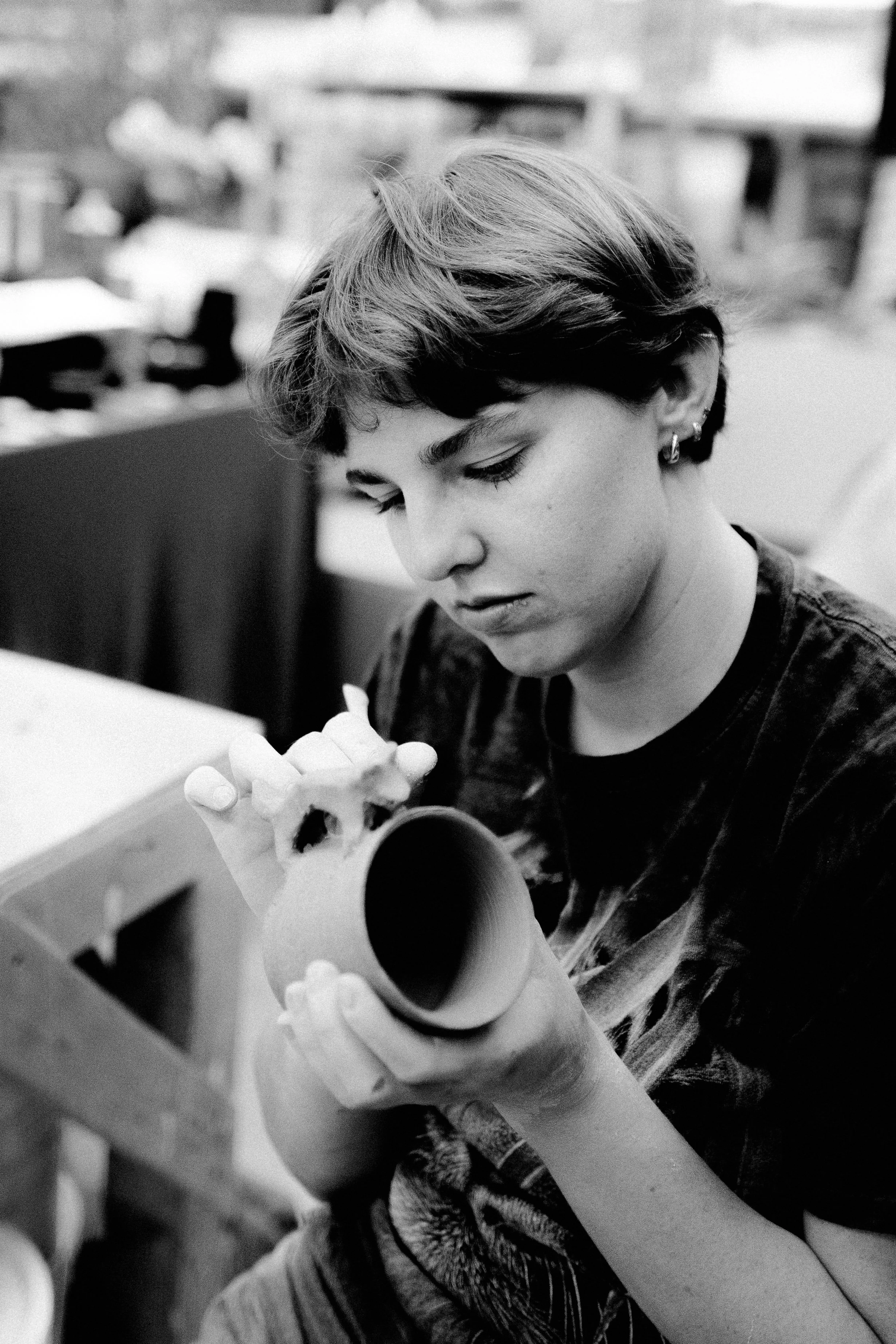Black and white photo of a person with short hair working on a craft project, holding a cardboard tube and a paper towel roll.