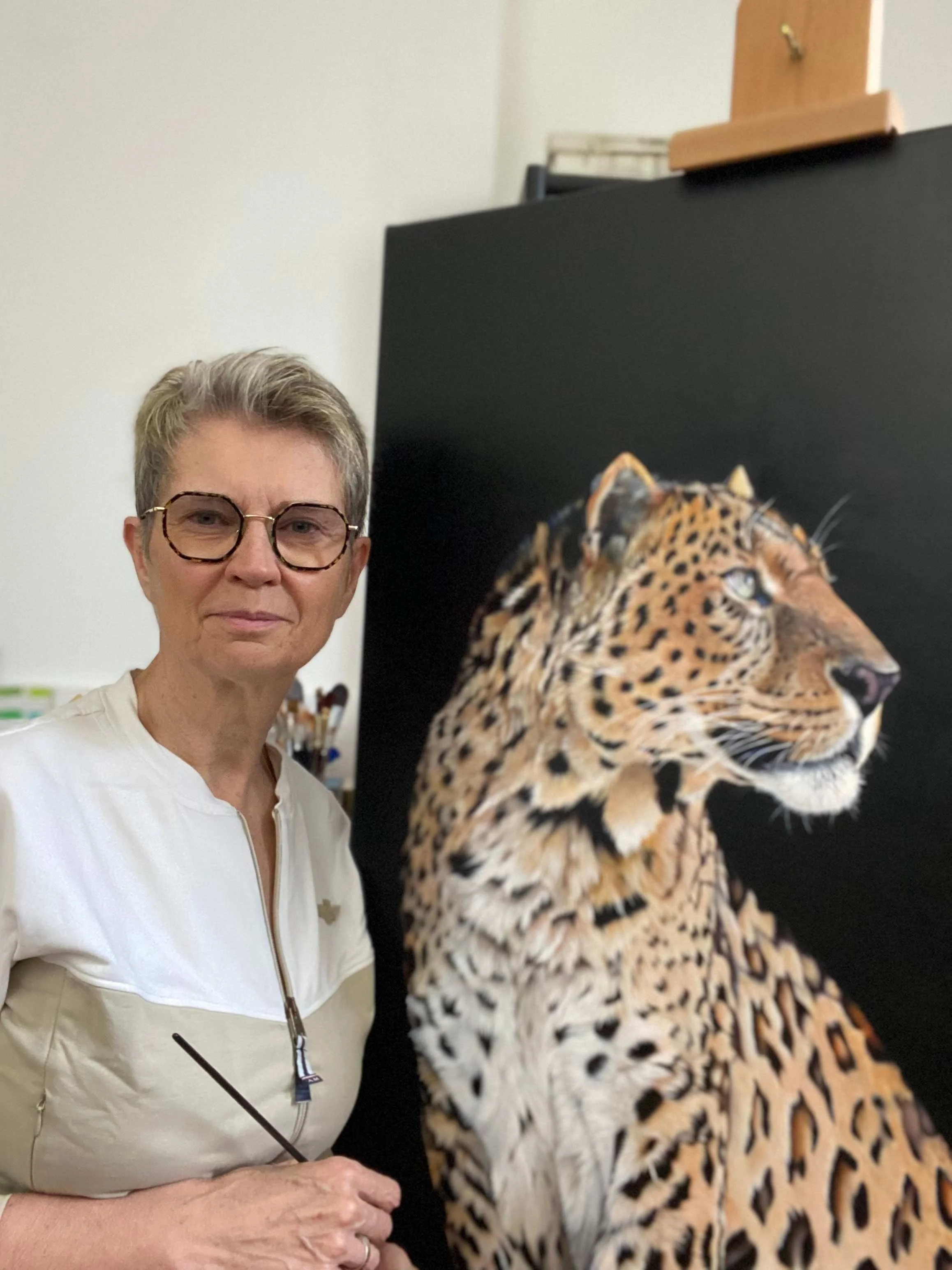 Lydia Mériaux, artiste peintre, dans son atelier posant devant son tableau représentant un léopard peint à l'acrylique — commande de portrait animalier personnalisé au pastel sec ou à l'acrylique
