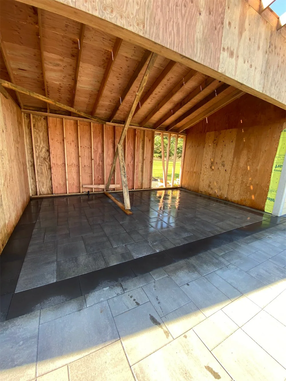 Construction site with wooden framing and partially installed black and gray tiles on the floor.