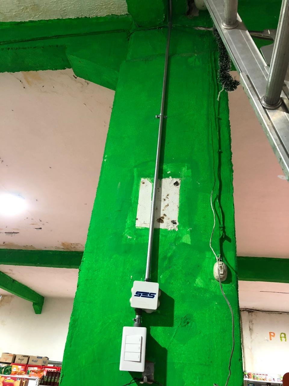Una toma vertical del cableado eléctrico en una pared de color verde, que incluye un conducto metálico, un regulador de velocidad, una caja con interruptores y cables sujetos con bridas.