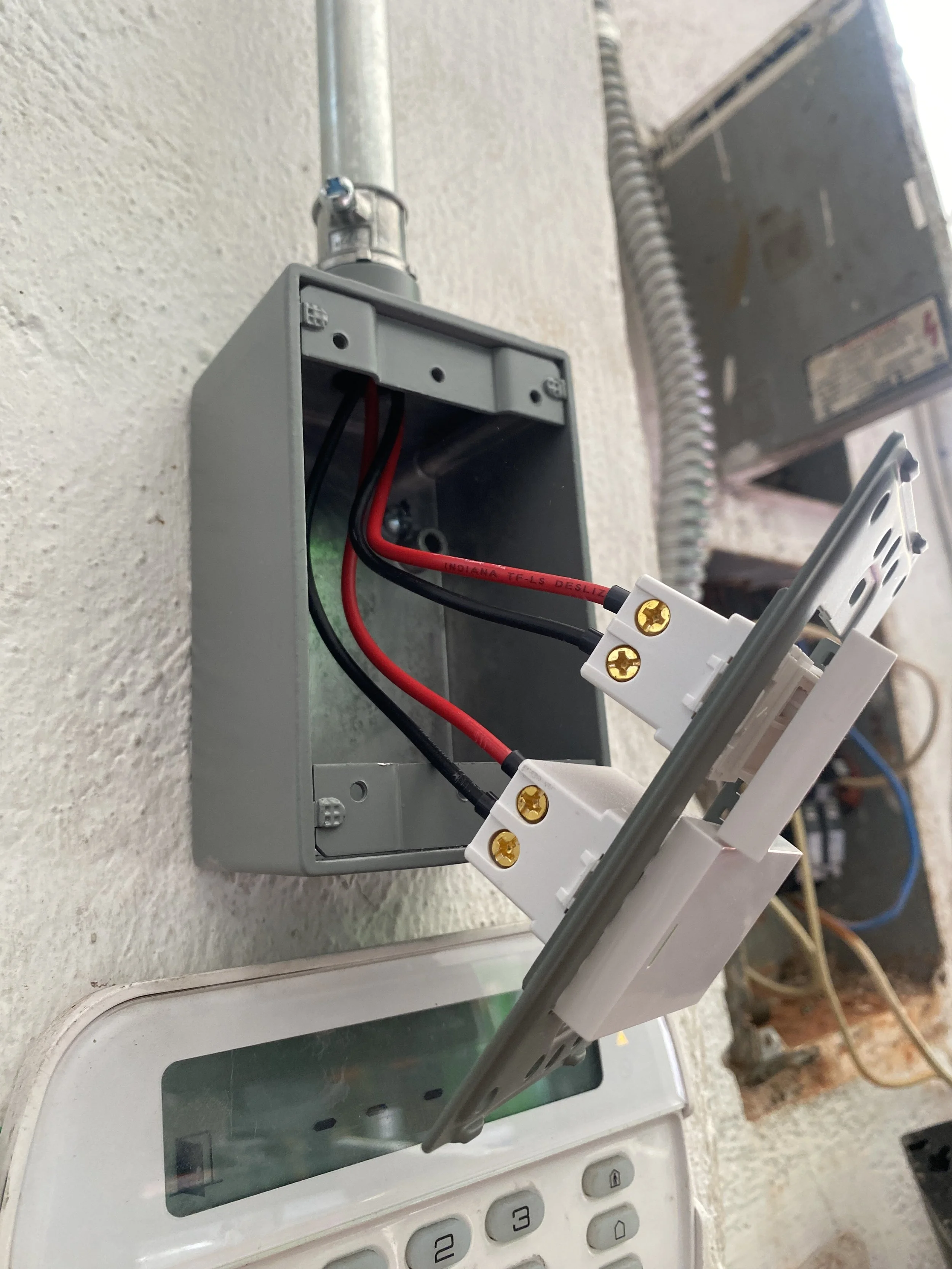 Cajón de distribución de energía eléctrica con cables rojos y negros conectados, instalado en una pared, cerca de un monitor y un teclado.