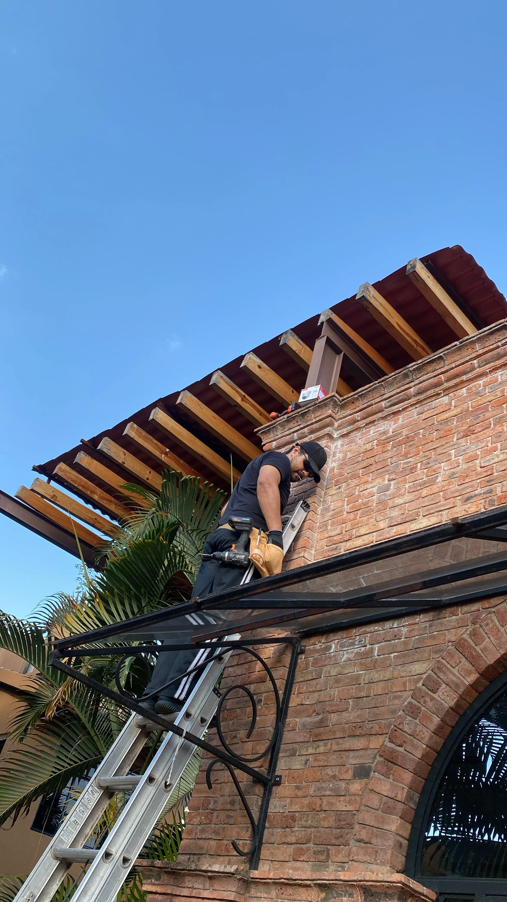 Un hombre trabaja en una remodelación en un edificio de ladrillo, usando una escalera y equipo de protección.