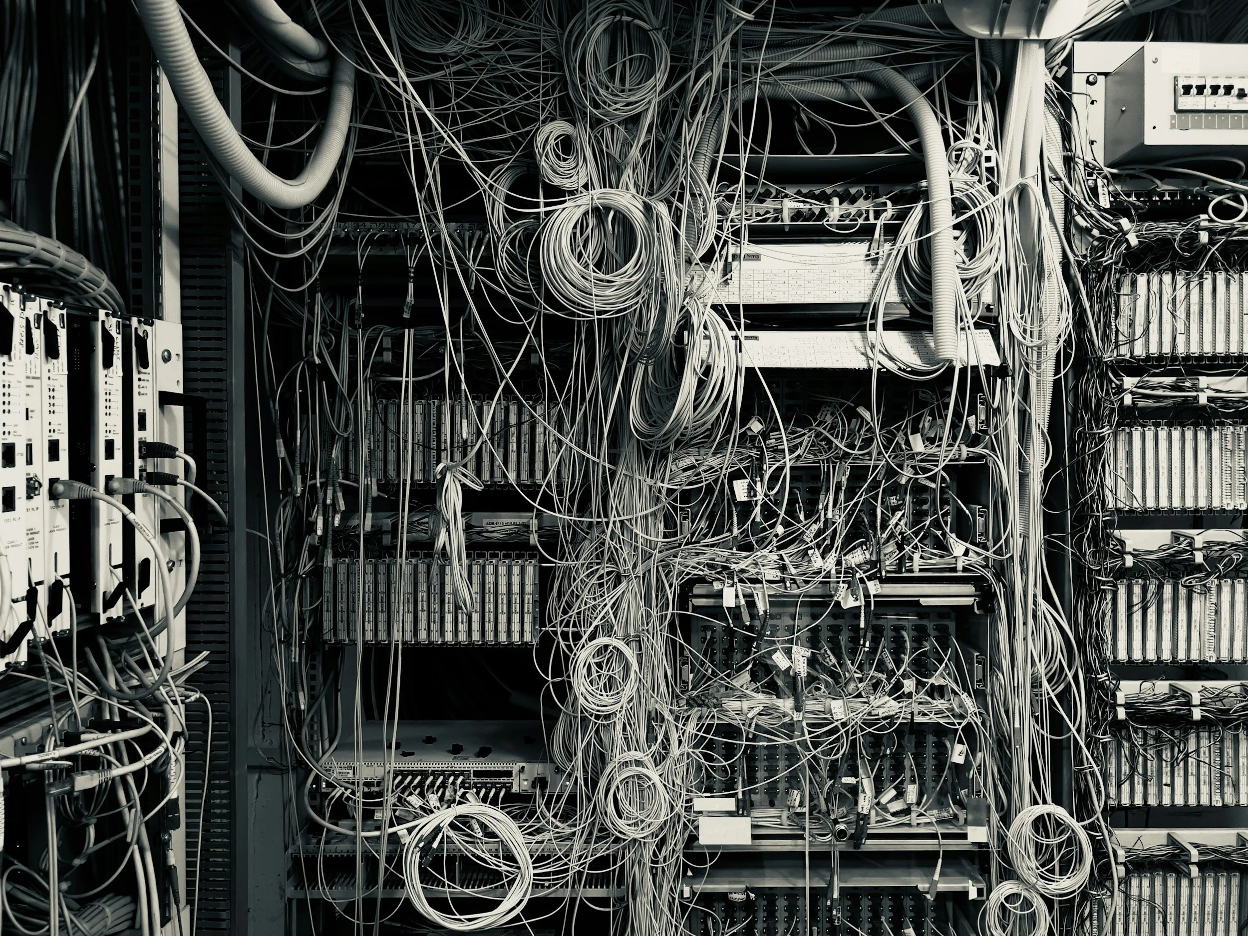 Imagen de un armario de servidores lleno de cables de red enredados, conectados a componentes y dispositivos electrónicos en un centro de datos.