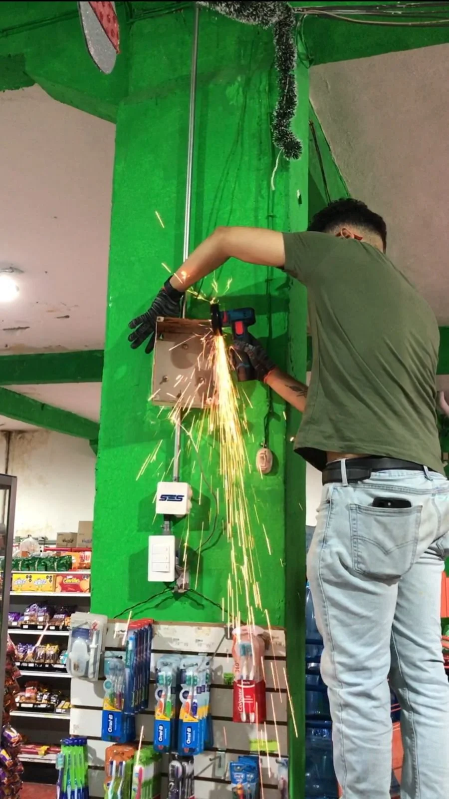Persona soldando un soporte metálico en una tienda, con chispas y gotas de fuego proyectadas.