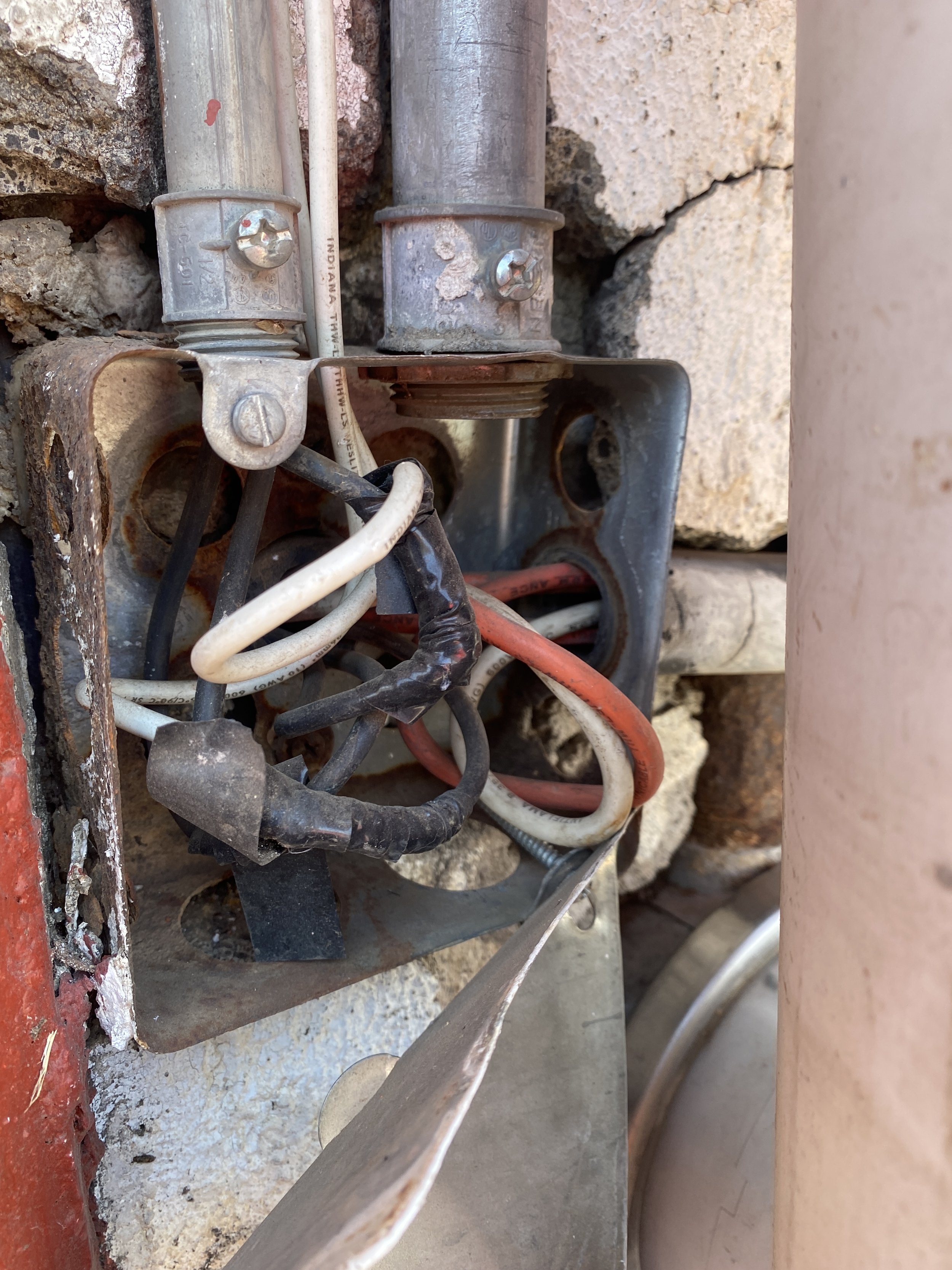 Conjunto de cables y conexiones eléctricas instaladas en una pared de piedra y cemento, con algunos componentes metálicos y tornillos visibles.