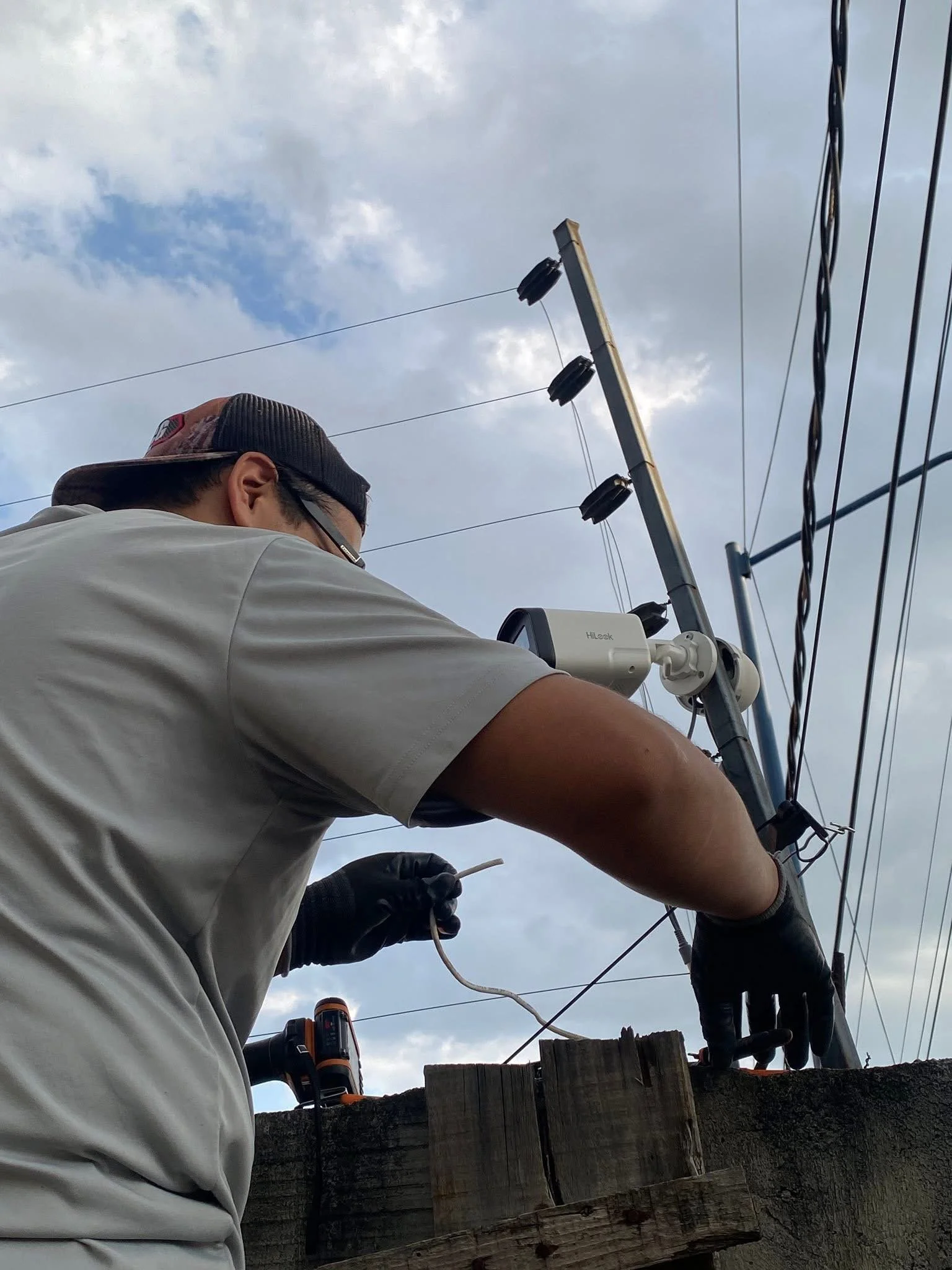 Persona trabajando en línea de transmisión eléctrica, con cielo nublado al fondo.