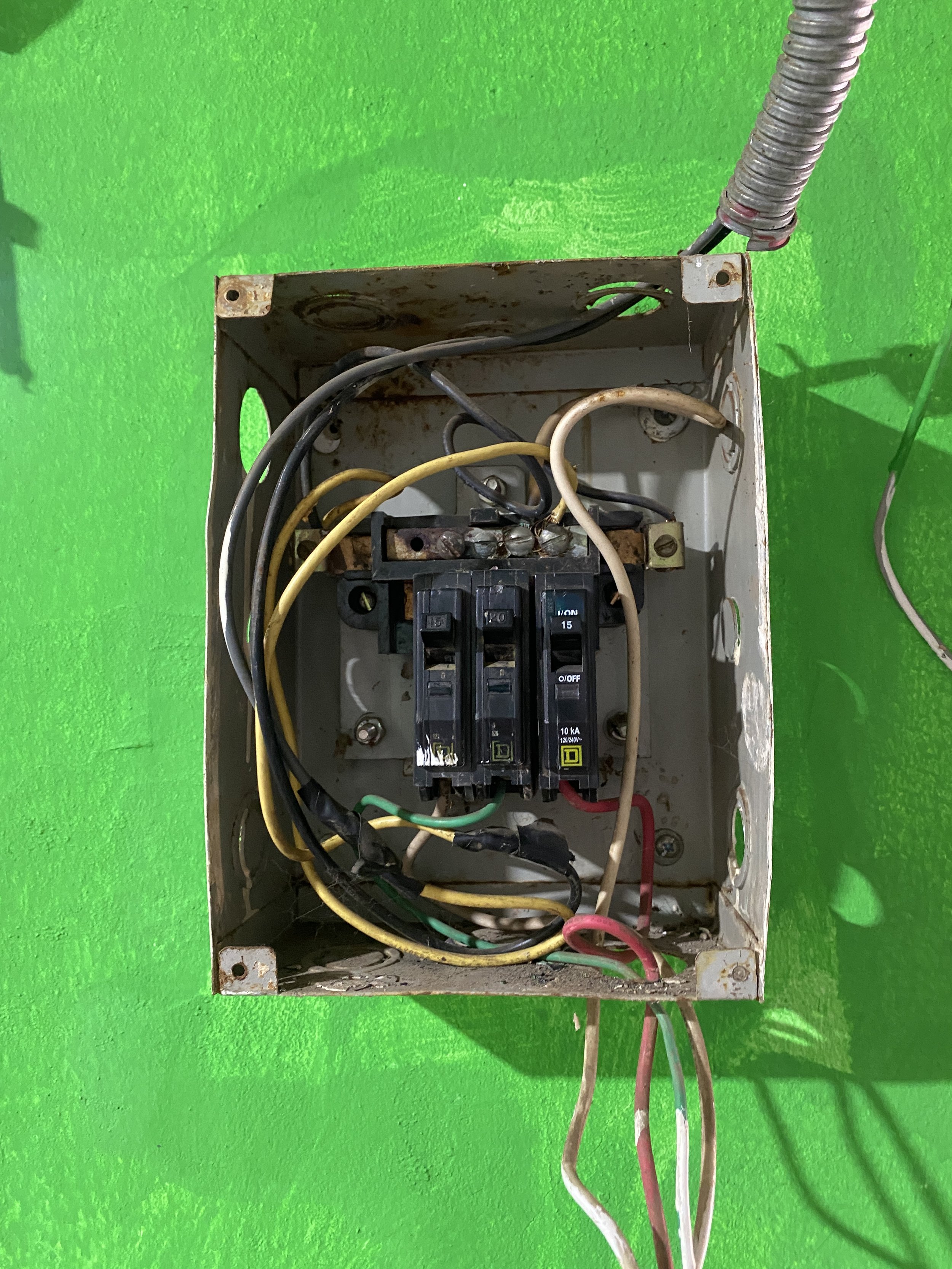 Caja eléctrica con cables conectados, sobre fondo de pared verde.