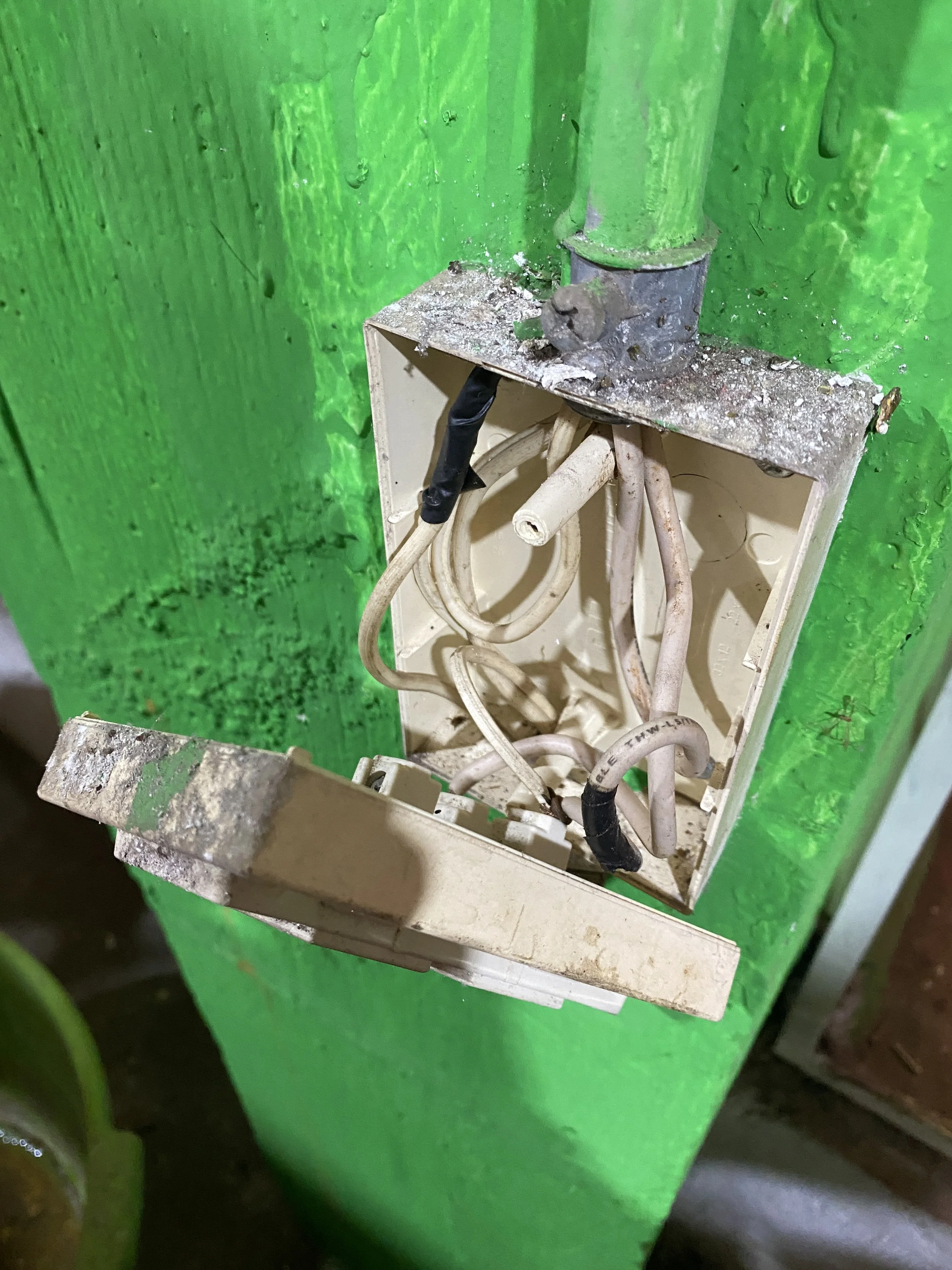 Un enchufe de pared viejo y sucio con cables desconectados, instalado en una pared pintada de verde.