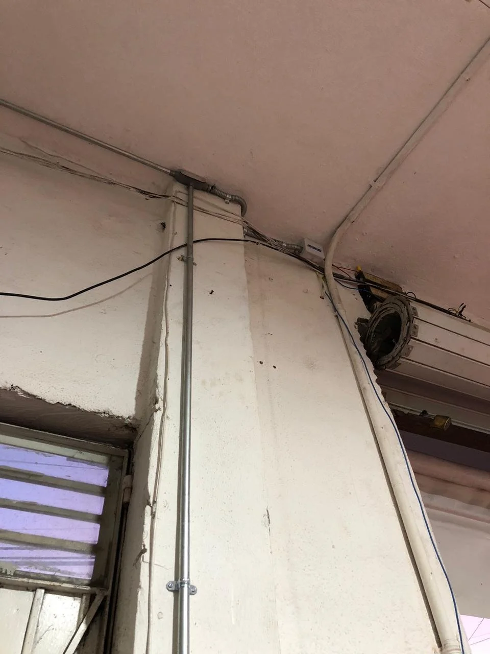 Cables y conductos eléctricos en la esquina de un techo de oficina con paredes blancas.