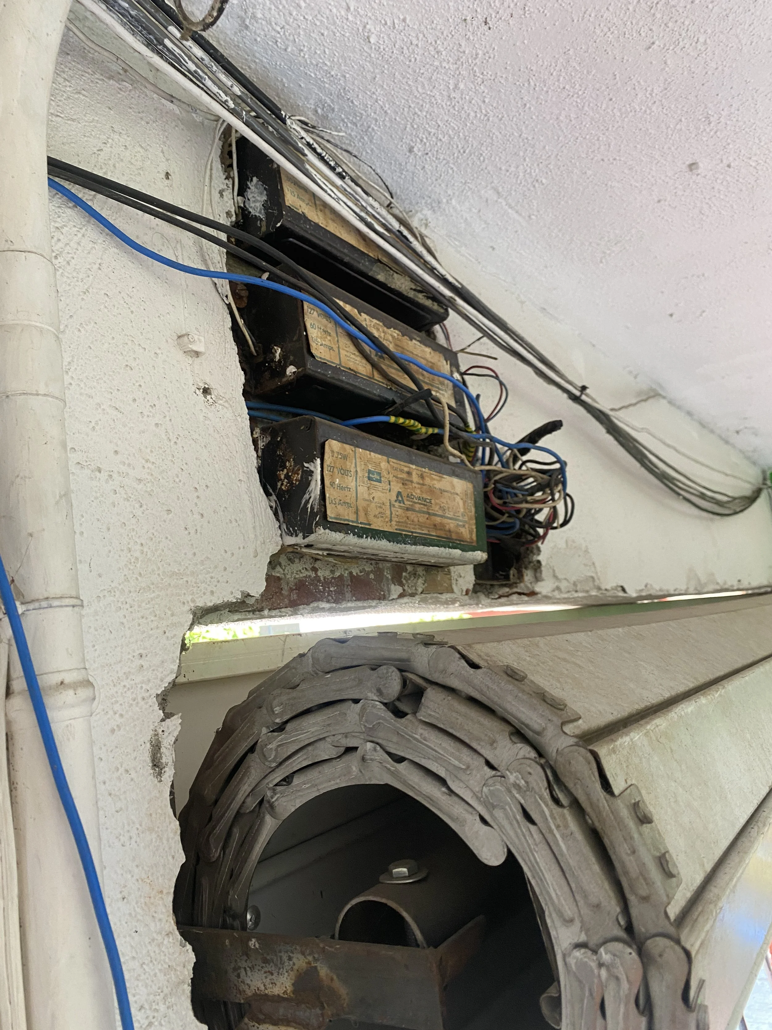 Una estructura de metal y cables eléctricos en una pared de cemento, con un neumático grande de tractor y partes de maquinaria antigua.
