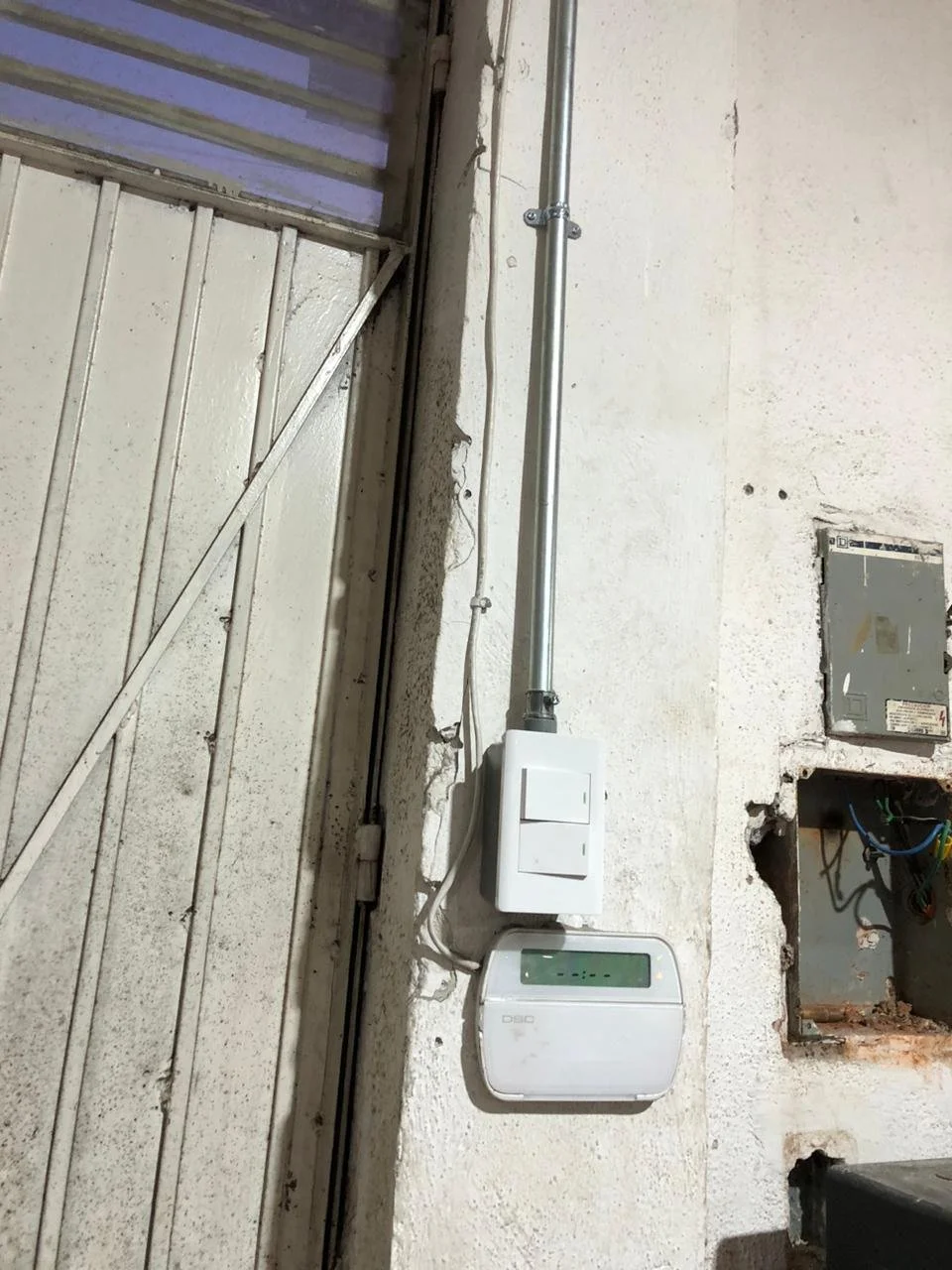 Instalación eléctrica en una pared, con un interruptor, un medidor y cables expuestos en una construcción.