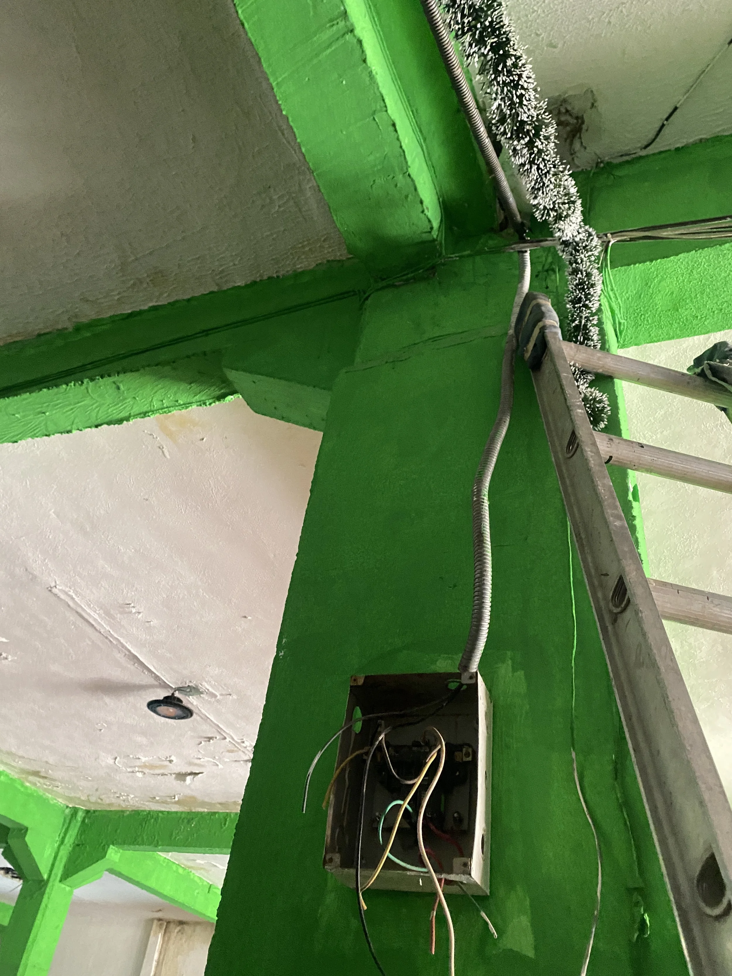 Vista de un techo en proceso de instalación eléctrica, con cables expuestos y un tablero eléctrico, en un espacio con paredes pintadas de verde y techos blancos.
