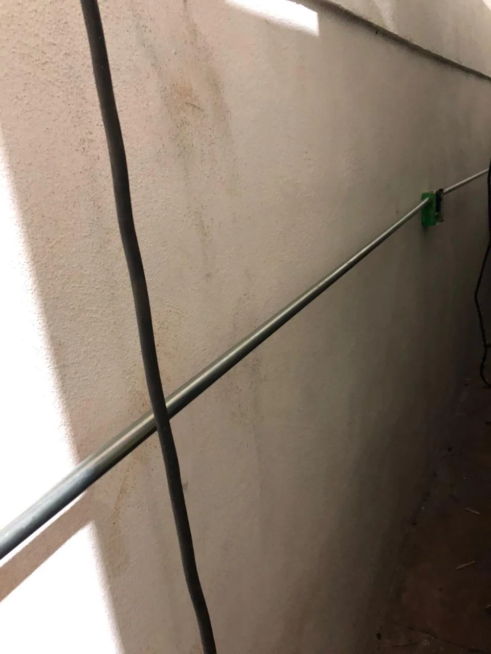 Imagen de una pared con una barra metálica horizontal y un cable negro colgado.