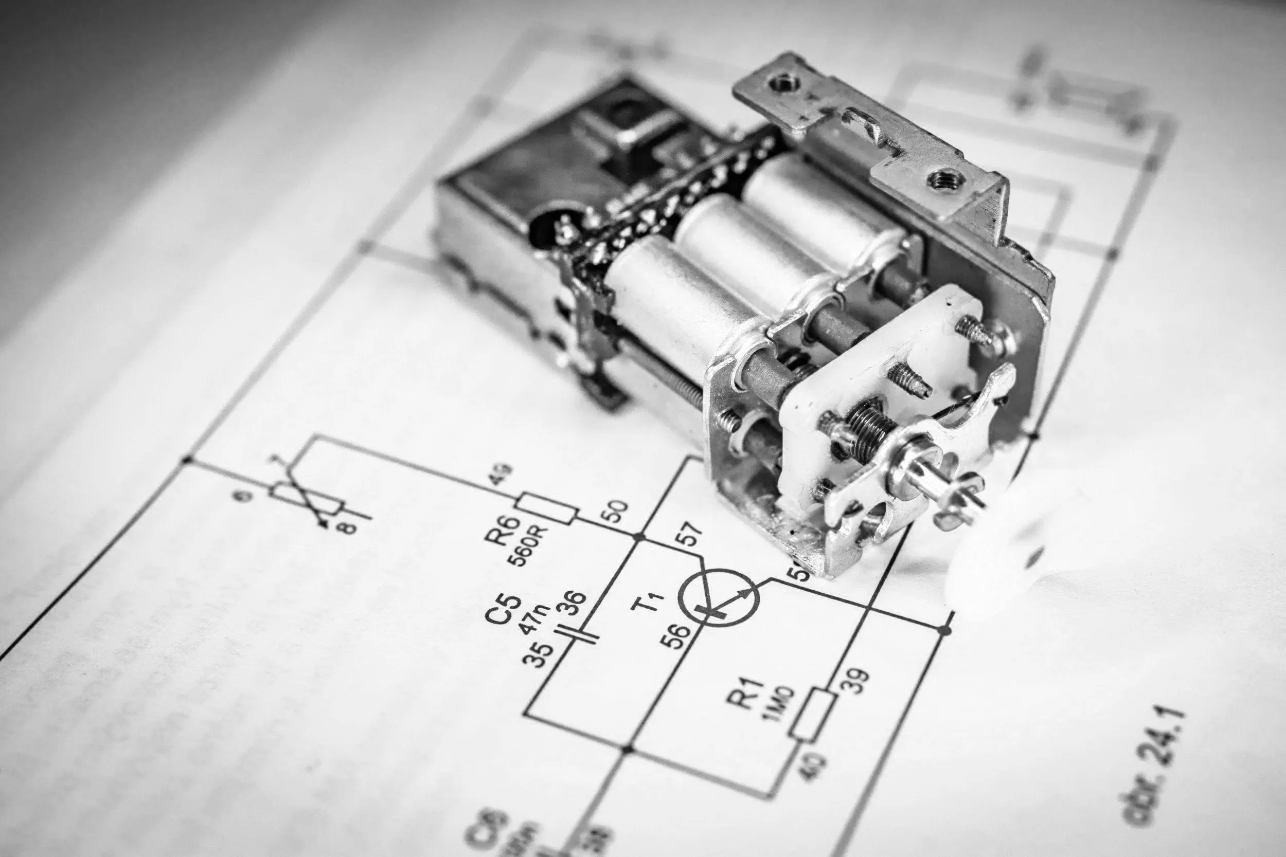 Imagen en blanco y negro de un motor paso a paso colocado sobre un esquema eléctrico. El esquema muestra diferentes componentes electrónicos y sus conexiones.