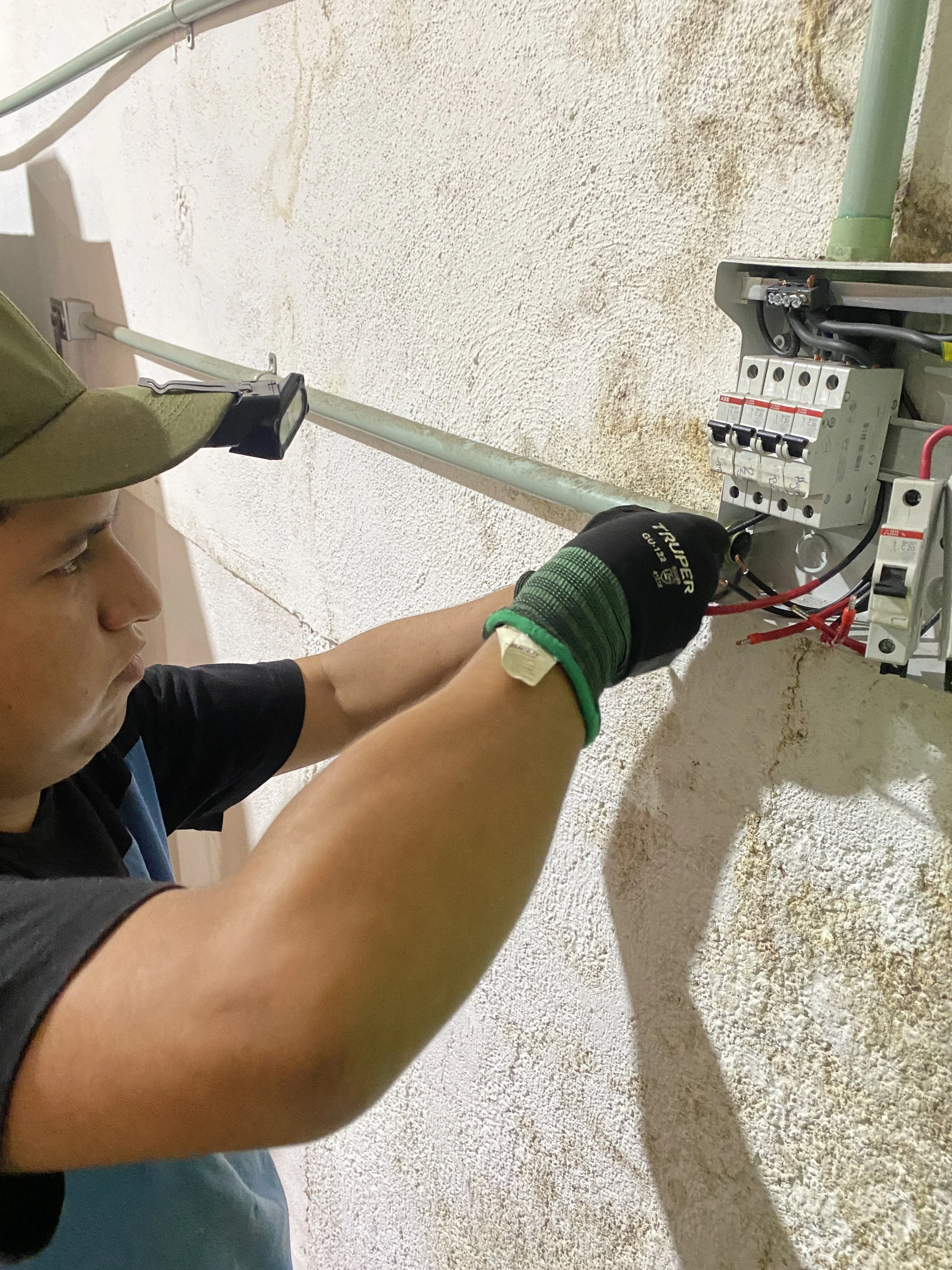 Persona trabajando en un panel eléctrico en una pared de concreto, usando guantes y protección ocular