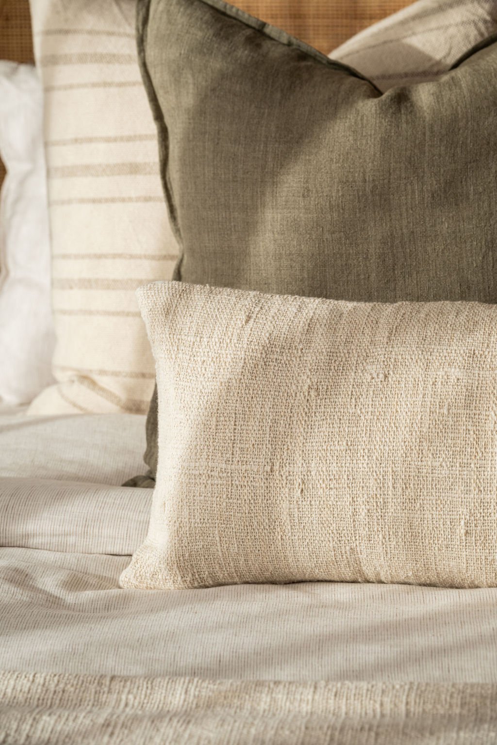 Close-up of a beige textured pillow resting on a bed with layered, neutral-toned pillows in the background.