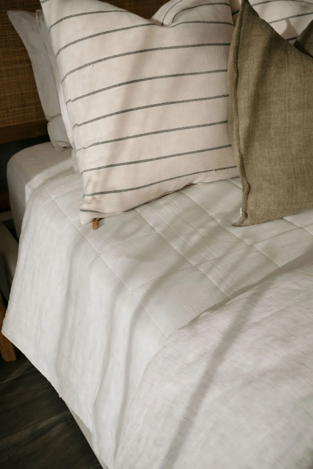 A bed with white bedding and three decorative pillows, including one striped and two solid-colored ones, in a cozy bedroom setting.