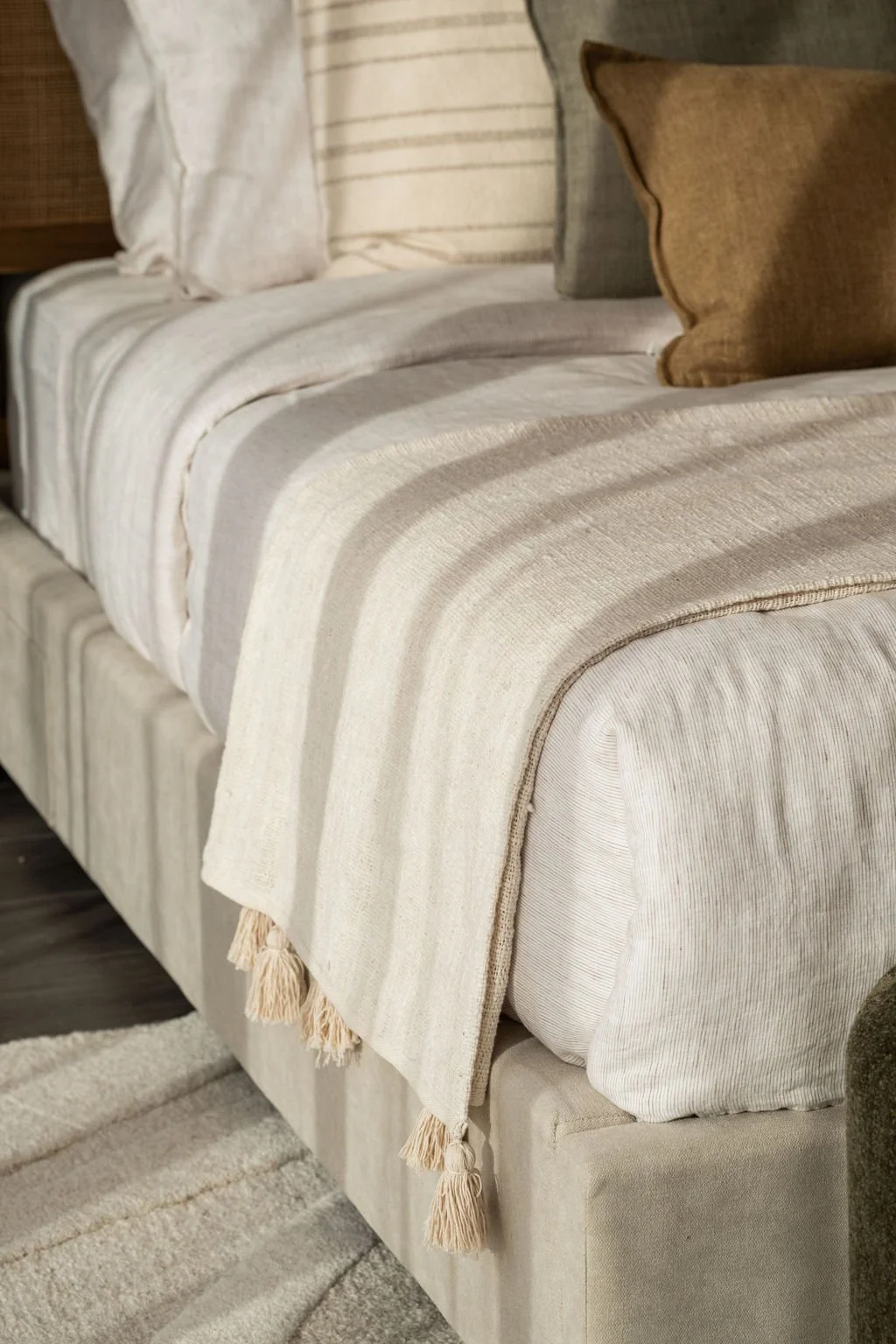 Close-up of a beige upholstered sofa with striped throw blanket and various pillows.