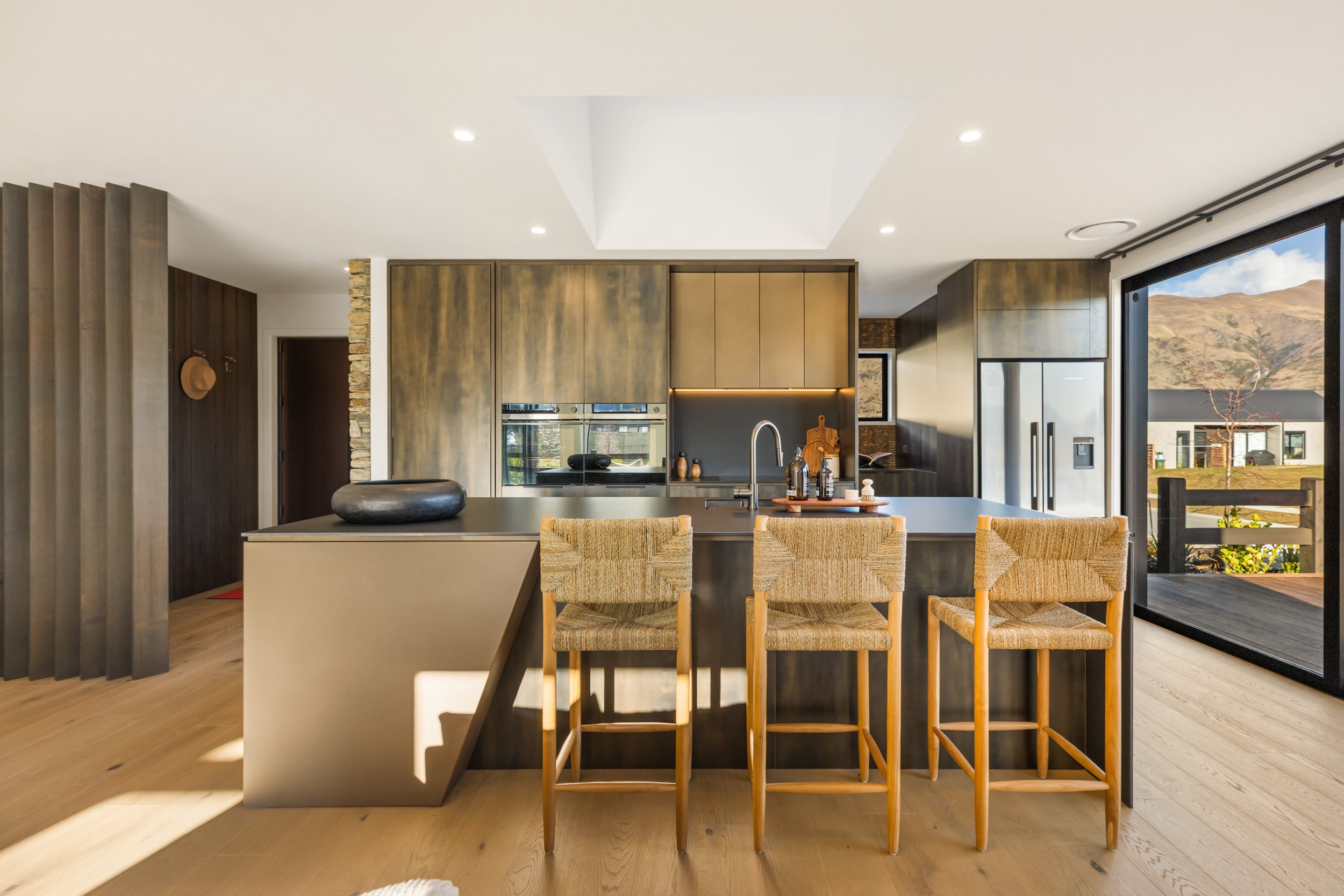 Modern kitchen with a black island, wooden cabinets, bar stools, and large sliding glass door with mountain view.