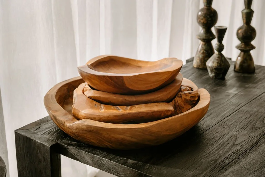 Stacked wooden bowls of varying sizes on a dark wooden table, with decorative vases in the background.