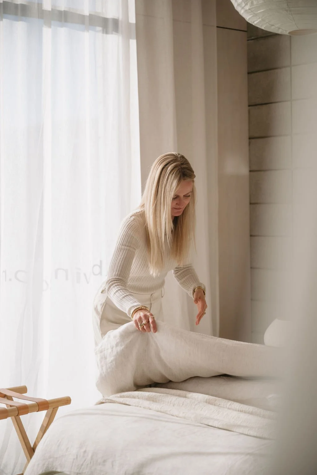 Owner of Wanaka Staging Studio making the bed with Weave Sova Savannah linen sheets in a bright room with beautiful sheer curtains.