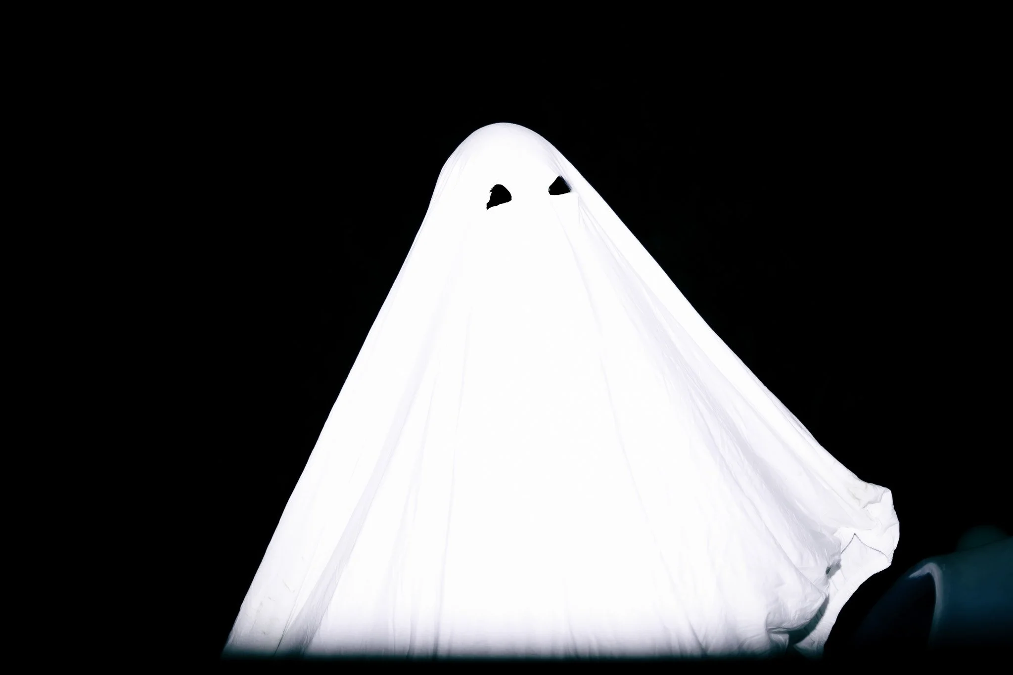 A ghost costume made from a white sheet with cut-out eyes, sitting on a dark background.