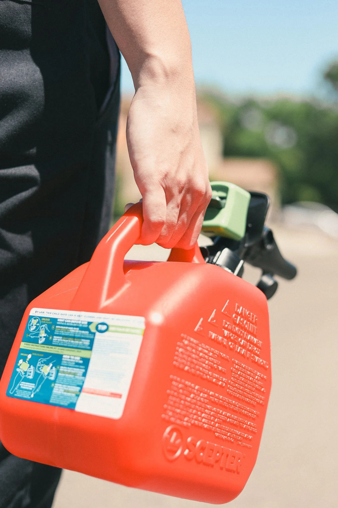 Close-up of a person holding a red gas canister with a green nozzle, outdoors on a sunny day.