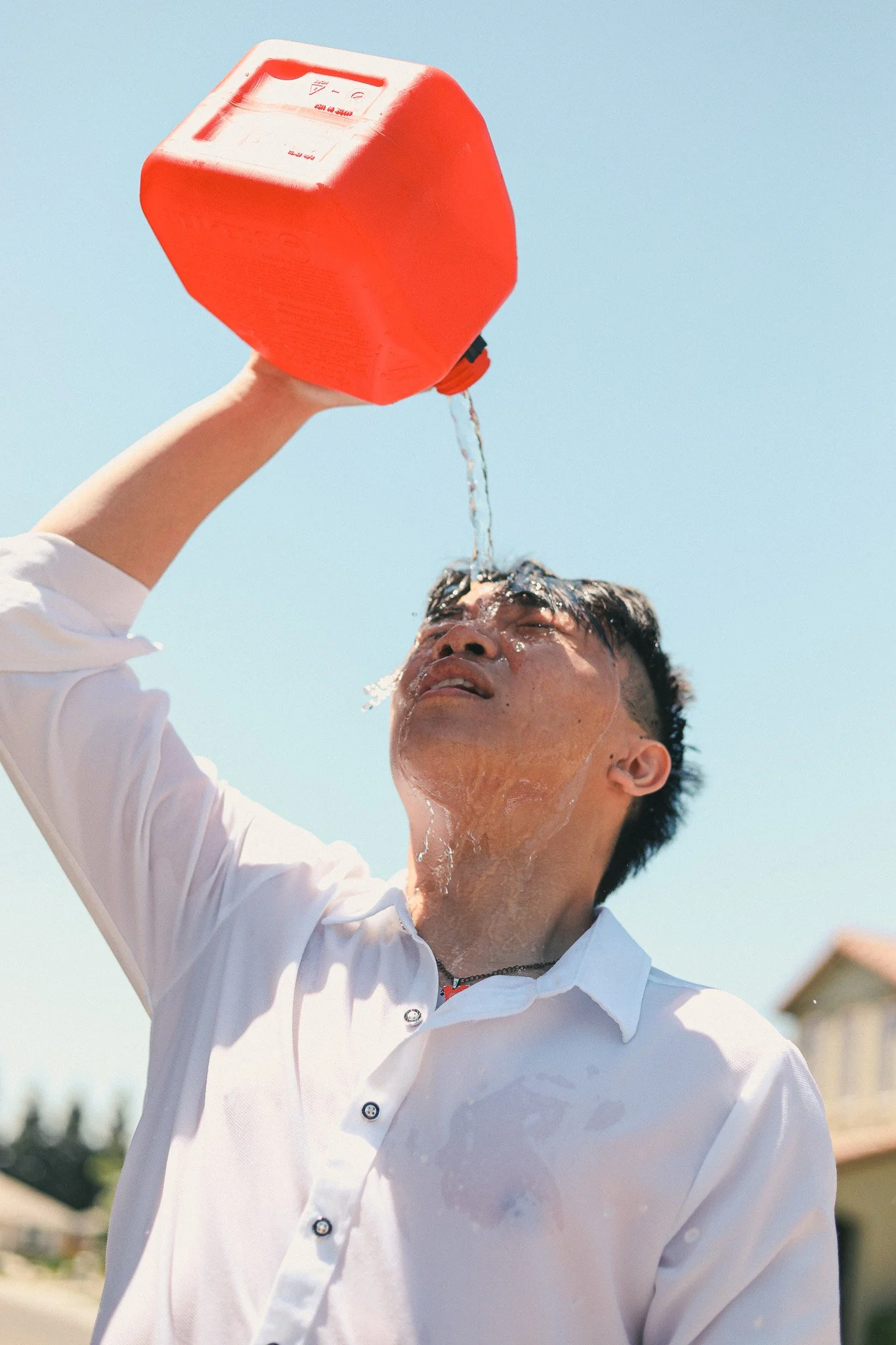 A man pouring water over his head from a red jerrycan outdoors on a sunny day.