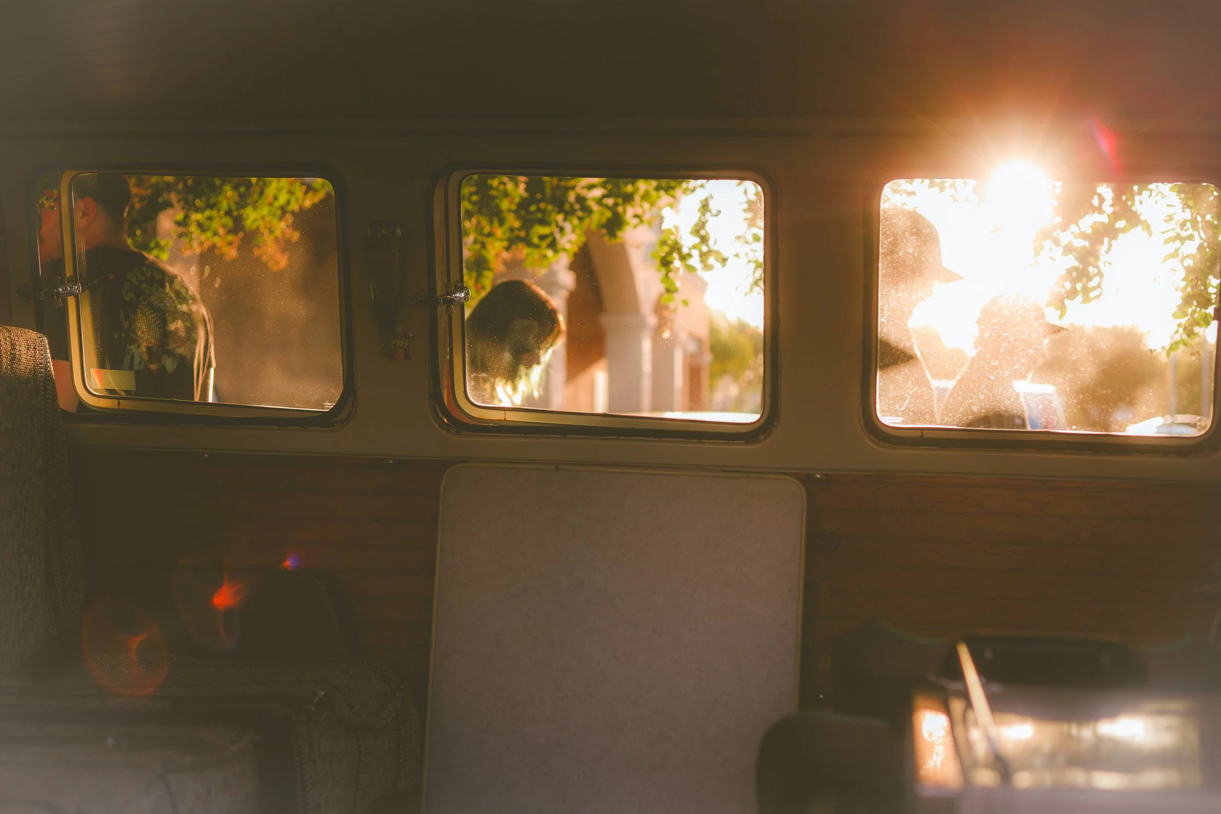 People standing outside, seen through the windows of a vintage van during sunset.