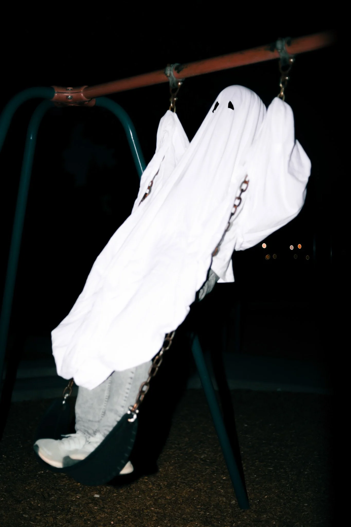 A swing set with a white sheet covering the seat, hanging outdoors at night.