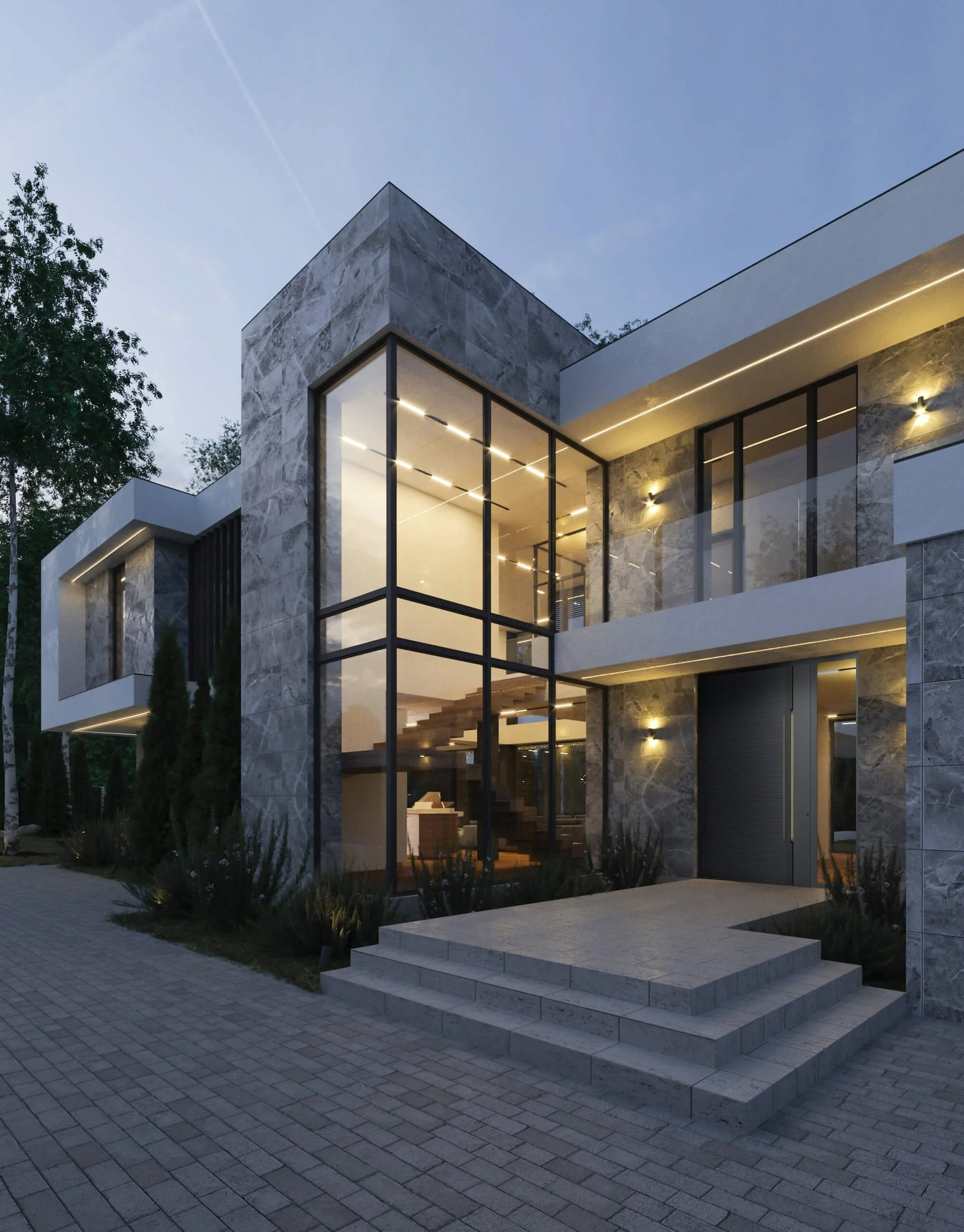 Modern house with large glass windows and stone exterior, illuminated exterior lighting, stairs leading to entrance, paved driveway, and surrounding trees at dusk.