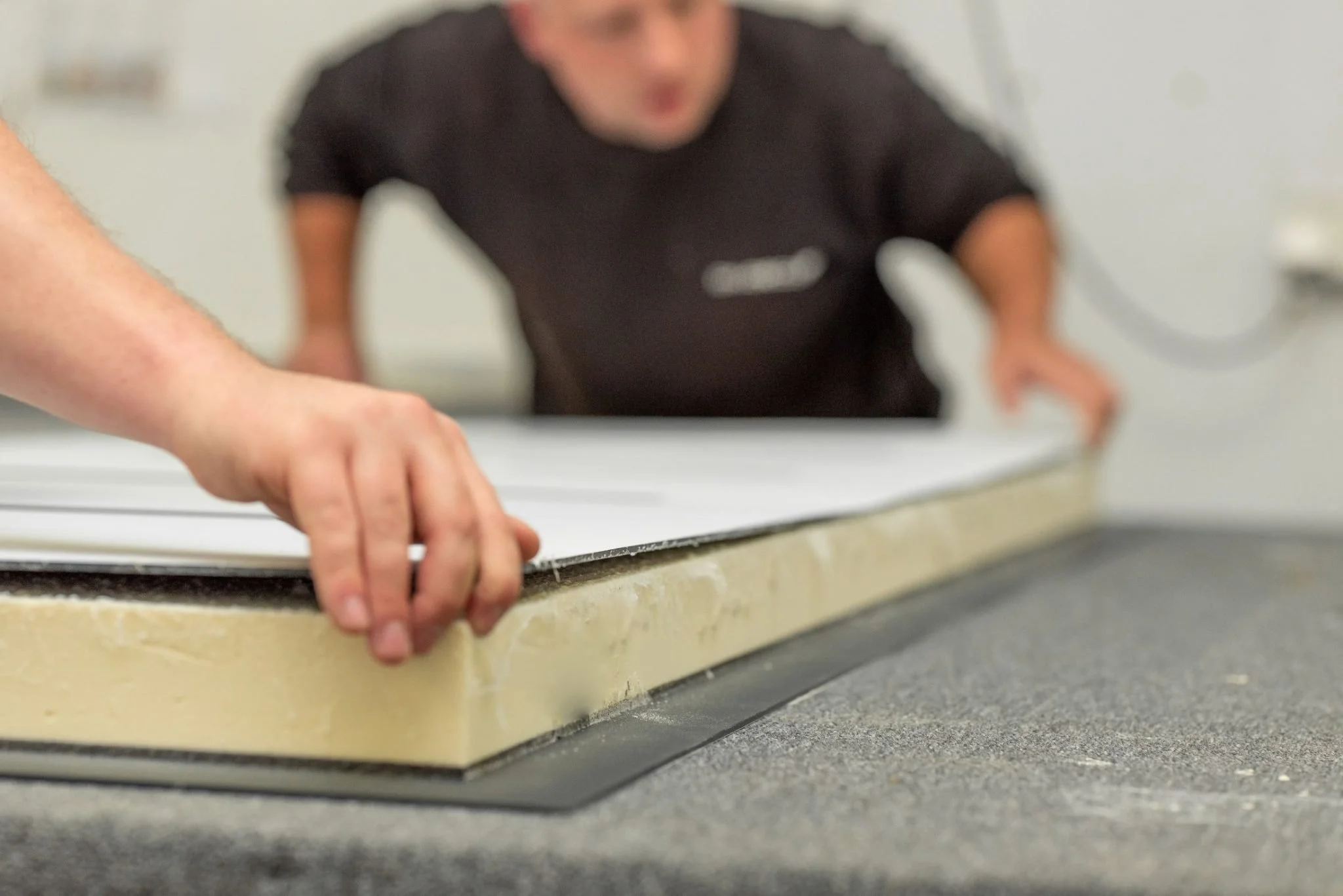 Close-up of a person's hand pressing a glass panel onto a foam insulation board during installation, with another person in the background observing.