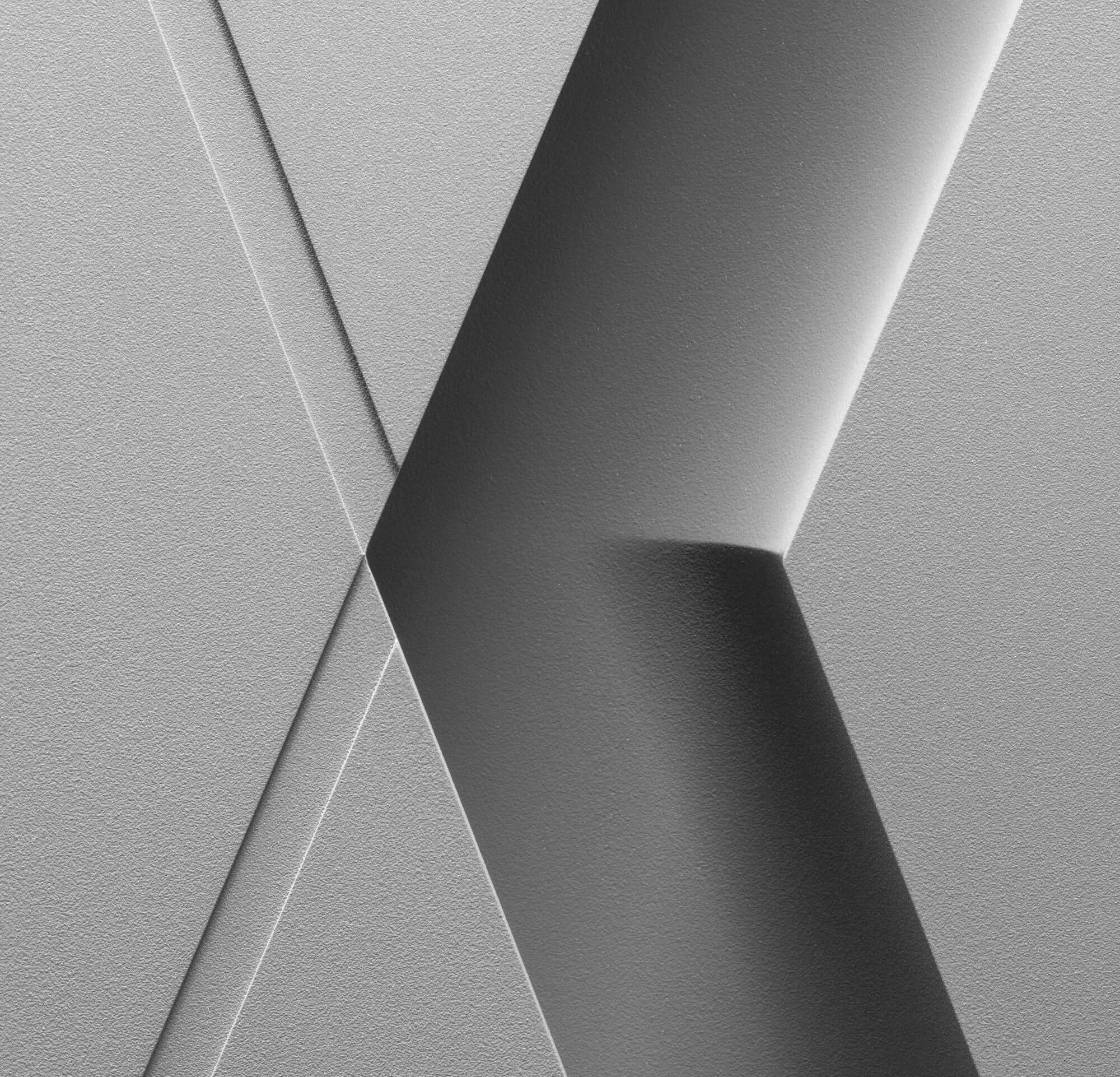 Close-up black and white photograph of textured architectural details, featuring intersecting lines and shadows.