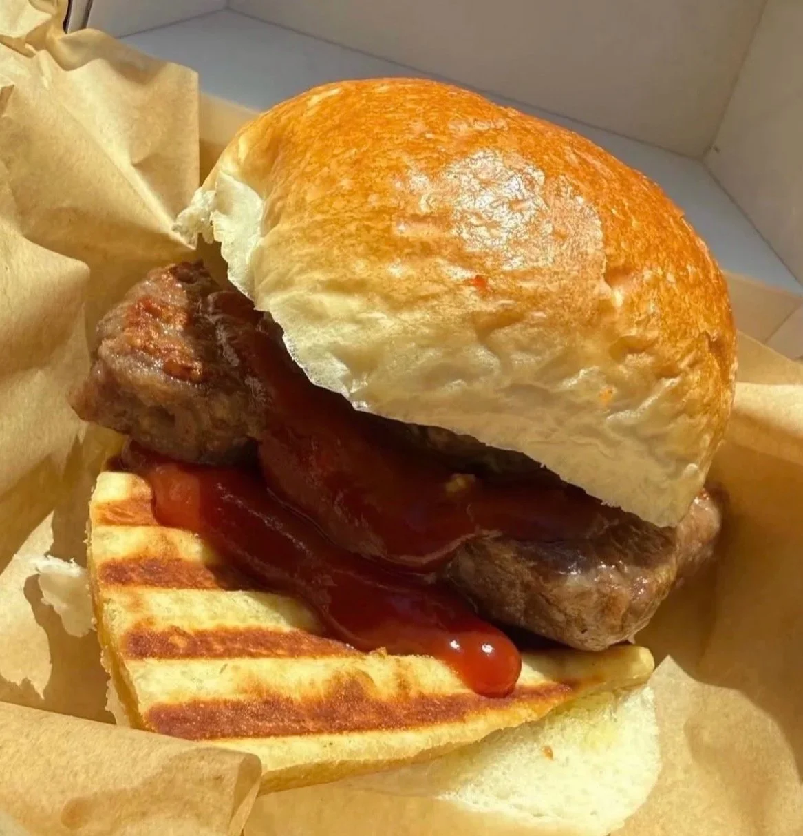 A close-up of a sandwich with grilled bread, a burger patty, bacon, and barbecue sauce.