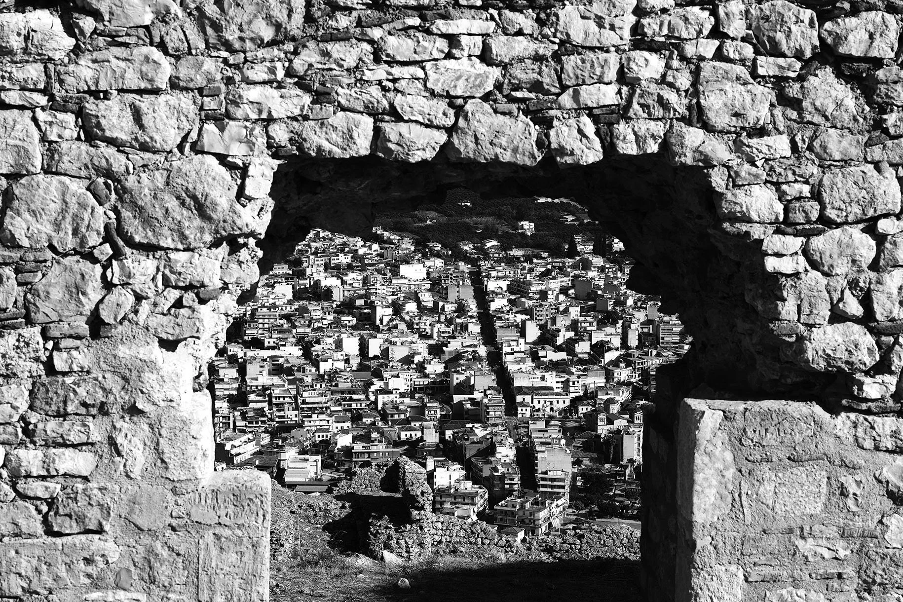 Vue d'une ville à travers une arche en pierre, en noir et blanc.