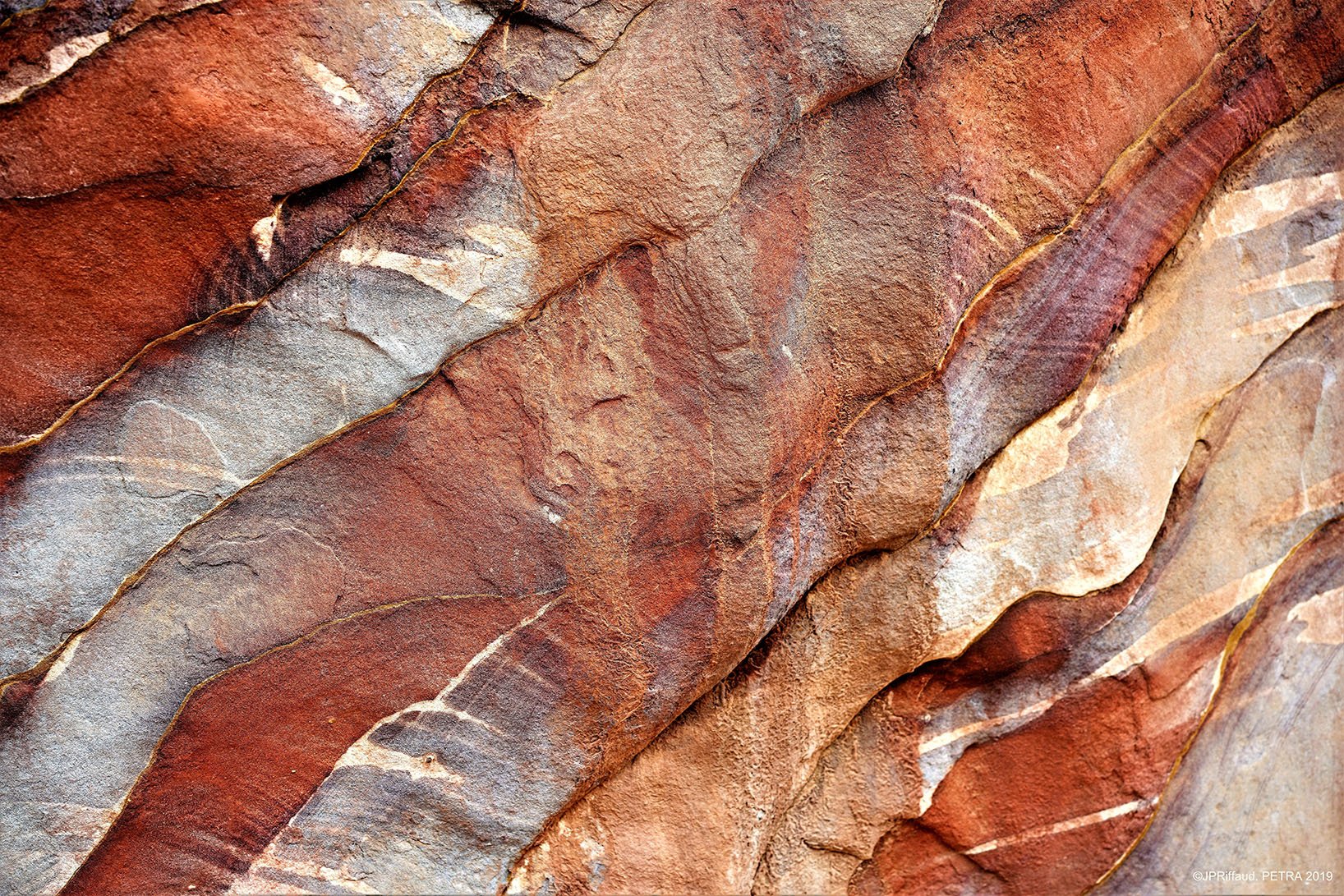 Surface rocheuse avec des stries rouges, brunes et grisâtres, formant des motifs naturels.