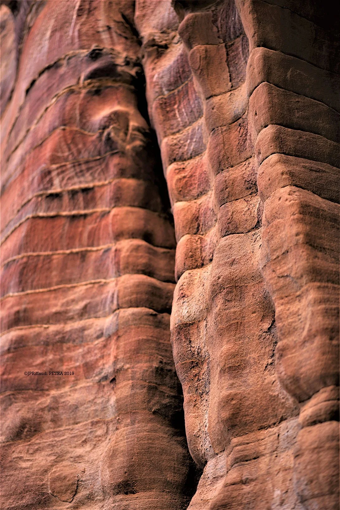 Zoom sur une paroi rocheuse en sandstone rouge et marron, avec des stries et des textures naturelles.