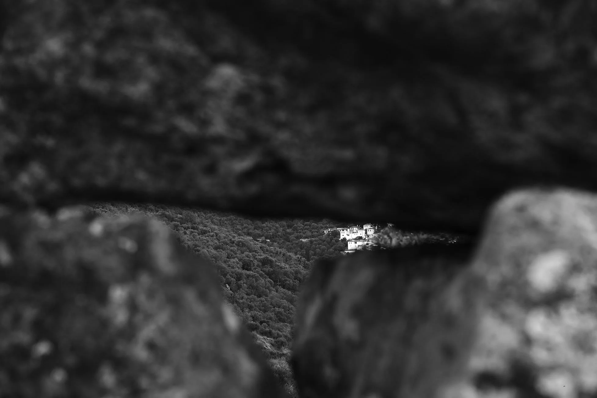 Vue d'un village blanc en haut d'une colline, vue à travers une ouverture dans des rochers ou des branches d'arbres.