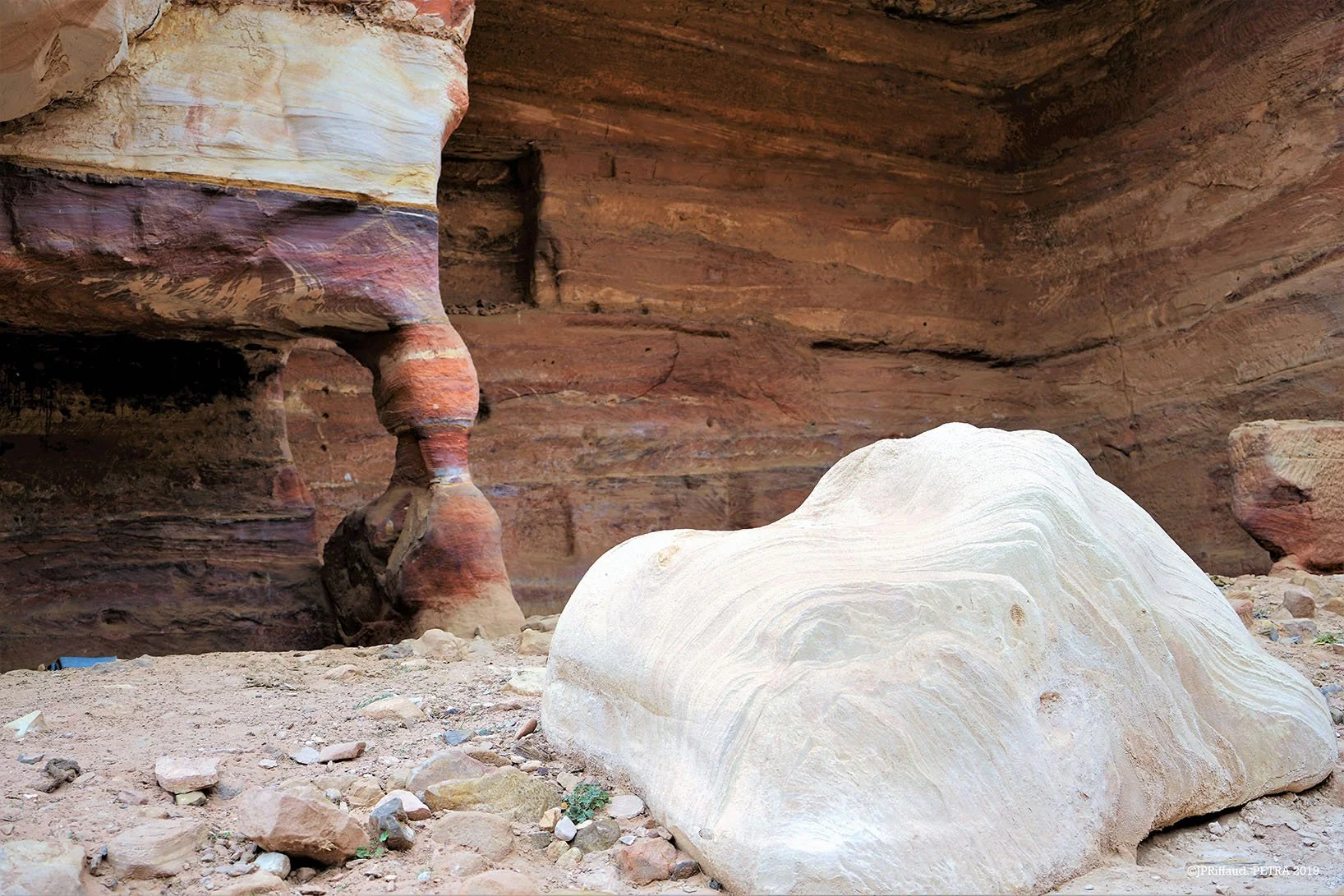 Gros rocher beige dans un canyon avec des murs rocheux aux teintes rouges, bruns et violettes.