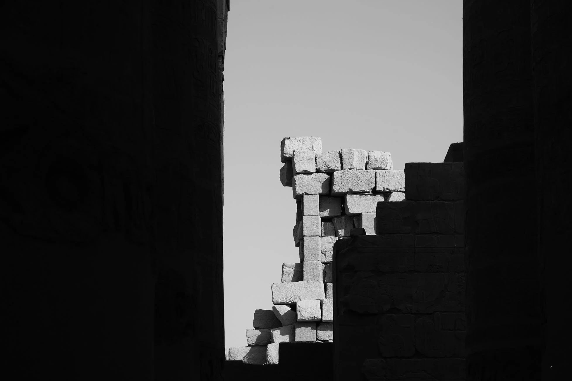 Mur blanc en pierre avec une ouverture, vue à travers un cadre formé par deux murs massifs dans un site archéologique antique.