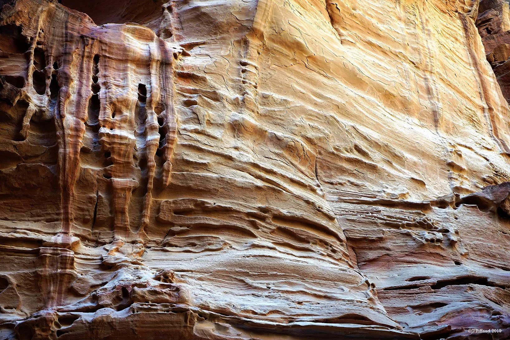 Paroi rocheuse avec des stries et des formations géologiques variées, couleurs allant du beige au brun