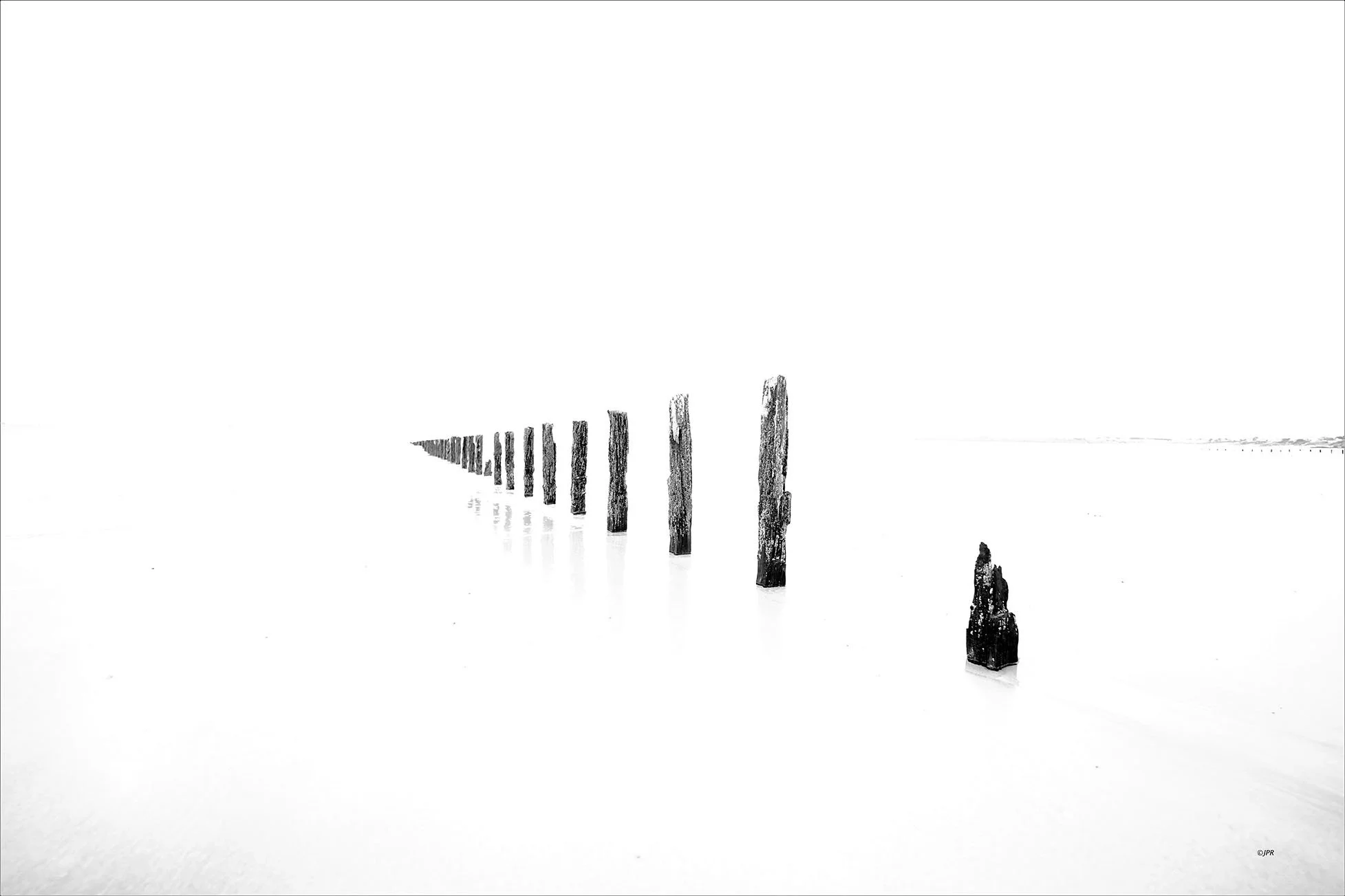 Une série de poteaux en bois émergeant d'une surface d'eau blanche et calme, s'étendant dans la distance.