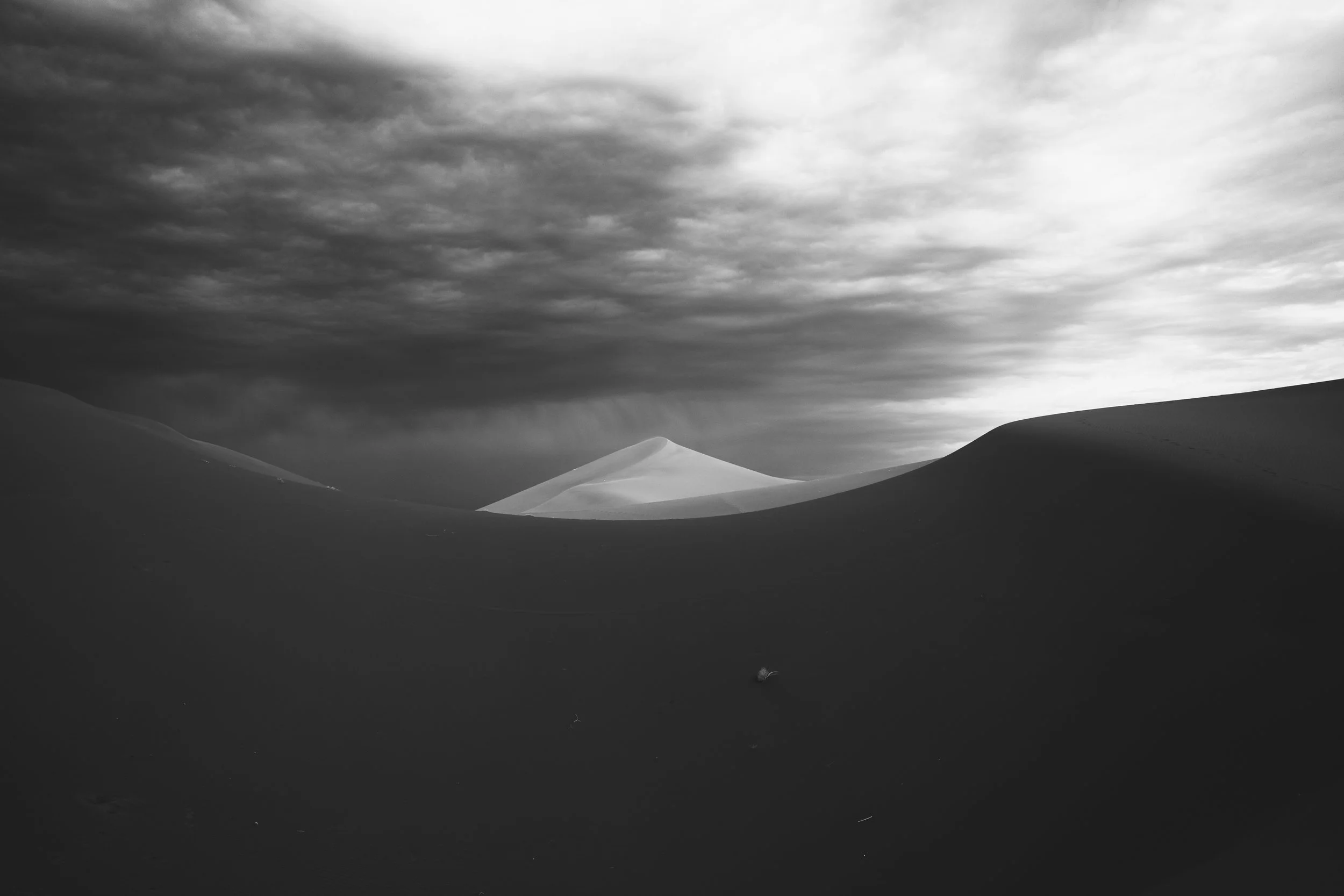 Paysage désertique avec des dunes de sable sous un ciel nuageux, en noir et blanc.