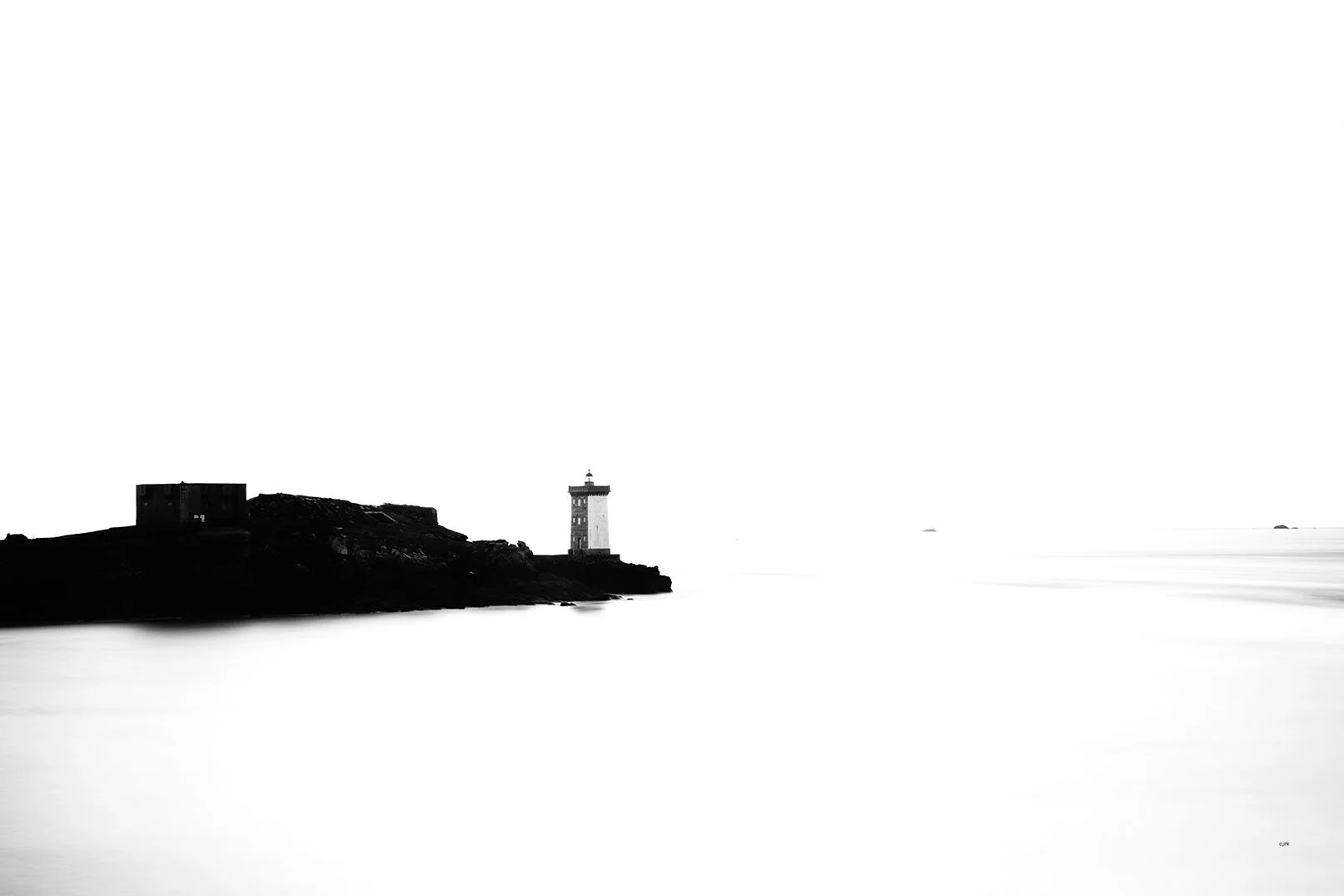 Silhouette de deux bâtiments sur une péninsule, avec une mer calme en premier plan, en noir et blanc.