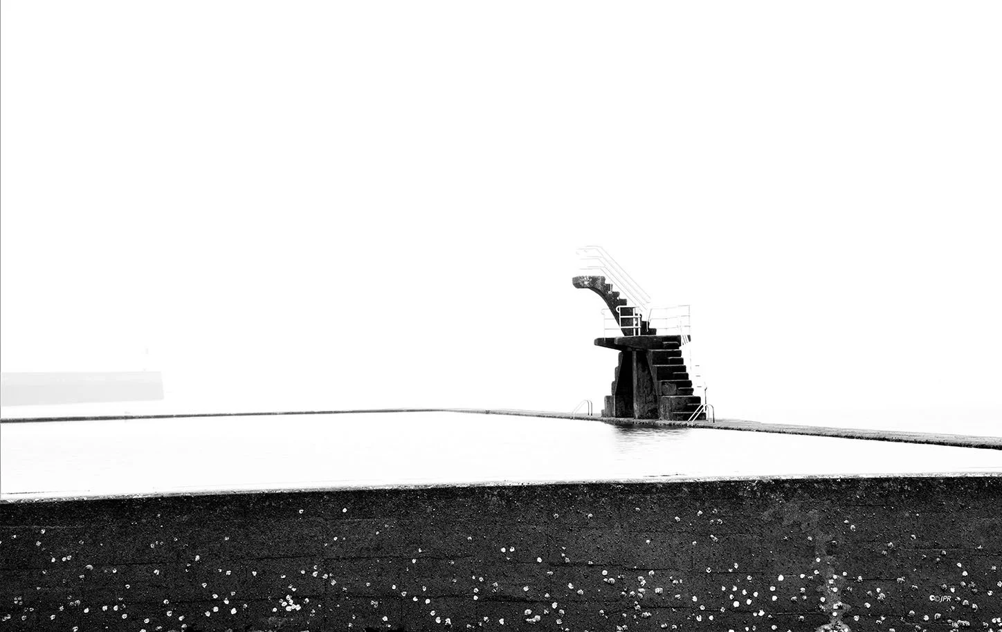 Une piscine vide avec une structure en béton à une extrémité, vue en noir et blanc.