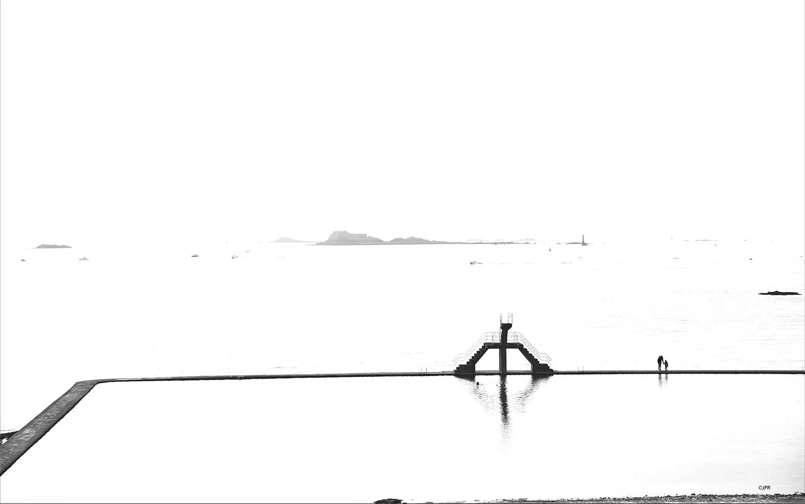 Une scène de la mer en noir et blanc avec une jetée ou un quai, deux personnes marchant côte à côte, et des îles ou des rochers à l'horizon.