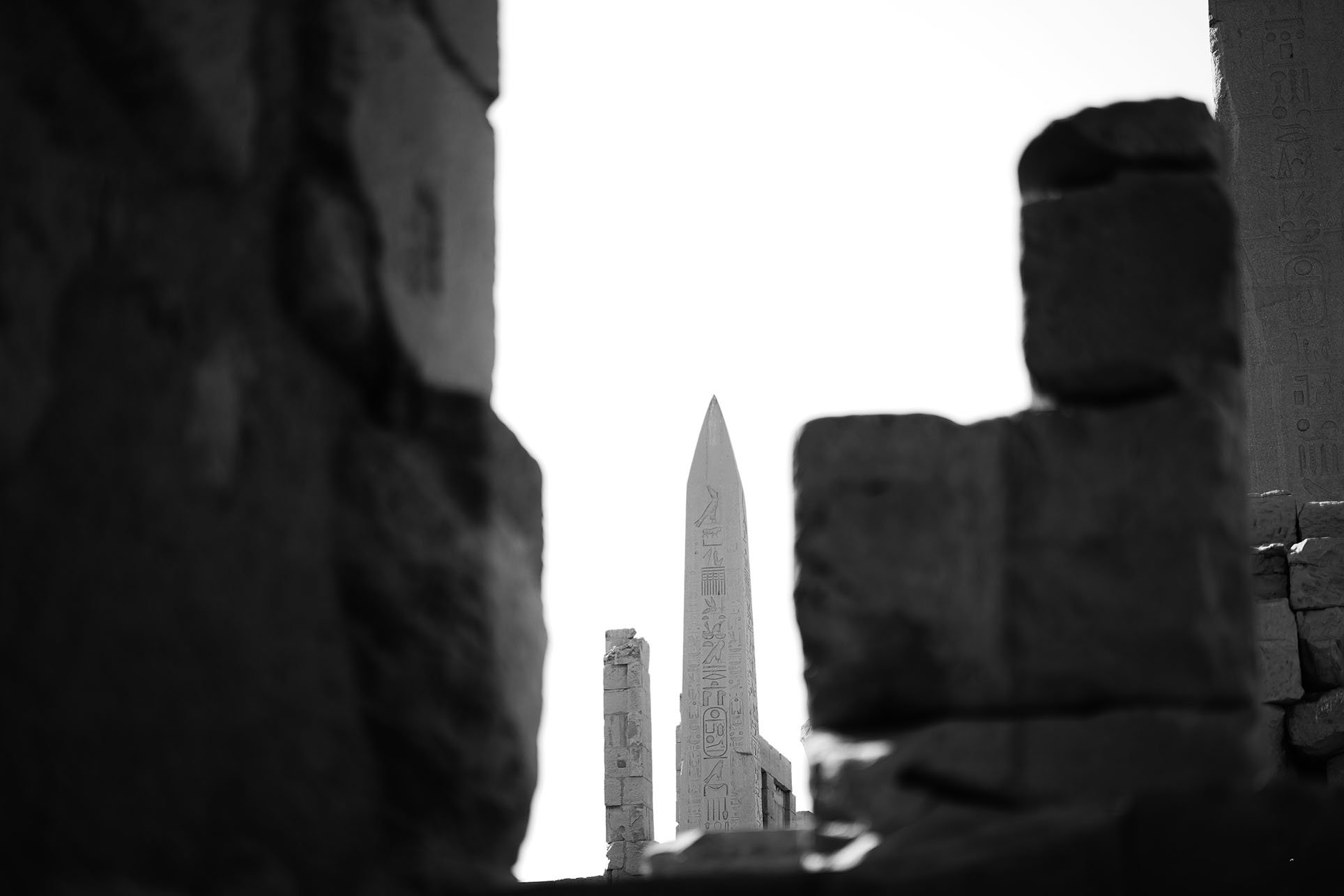 Obélisque égyptien avec hiéroglyphes, vu à travers une ouverture dans un mur en pierre.