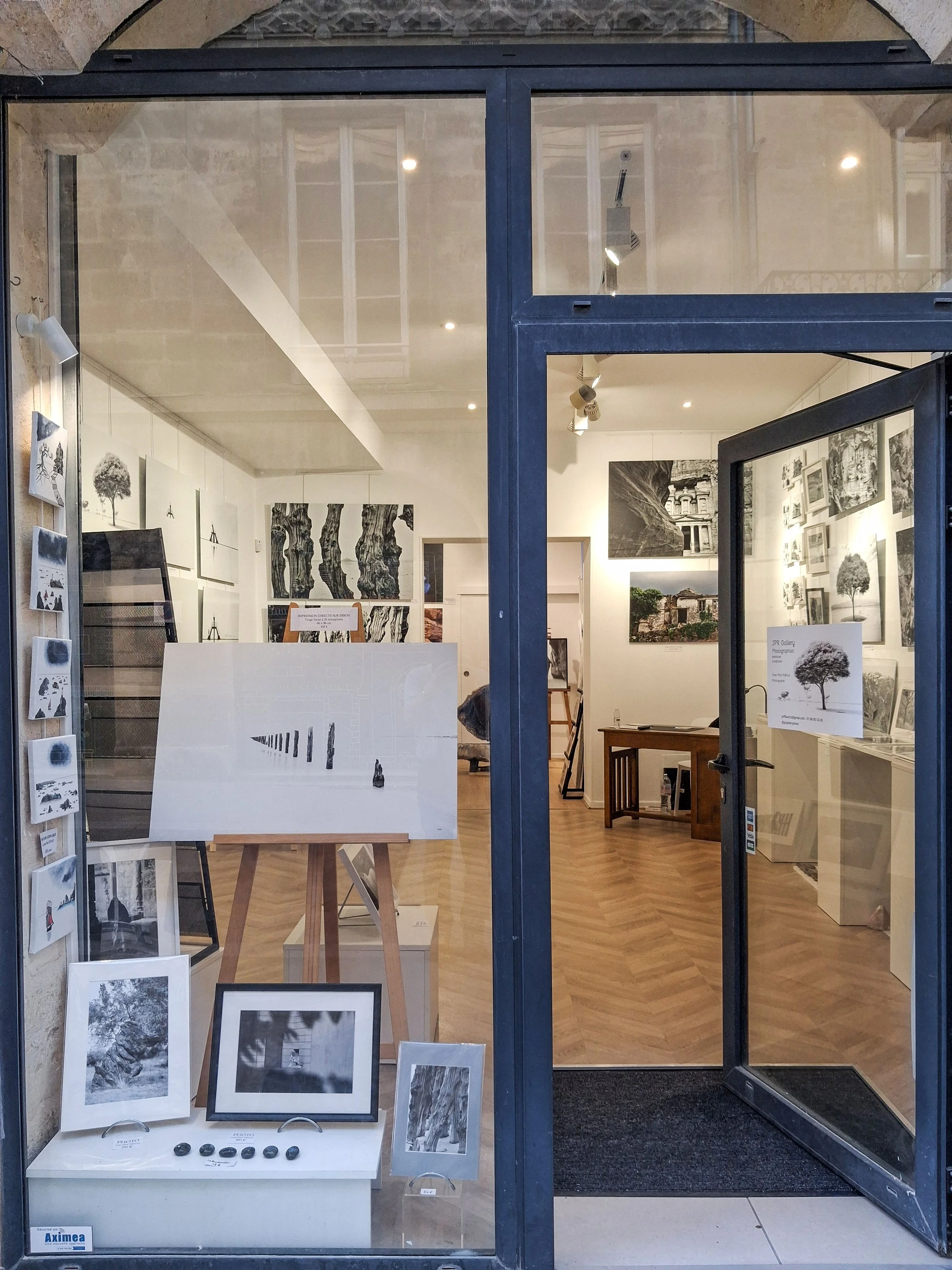 Vue de la devanture d'une galerie d'art avec des œuvres d'art en noir et blanc exposées à l'intérieur, visibles à travers la vitre.