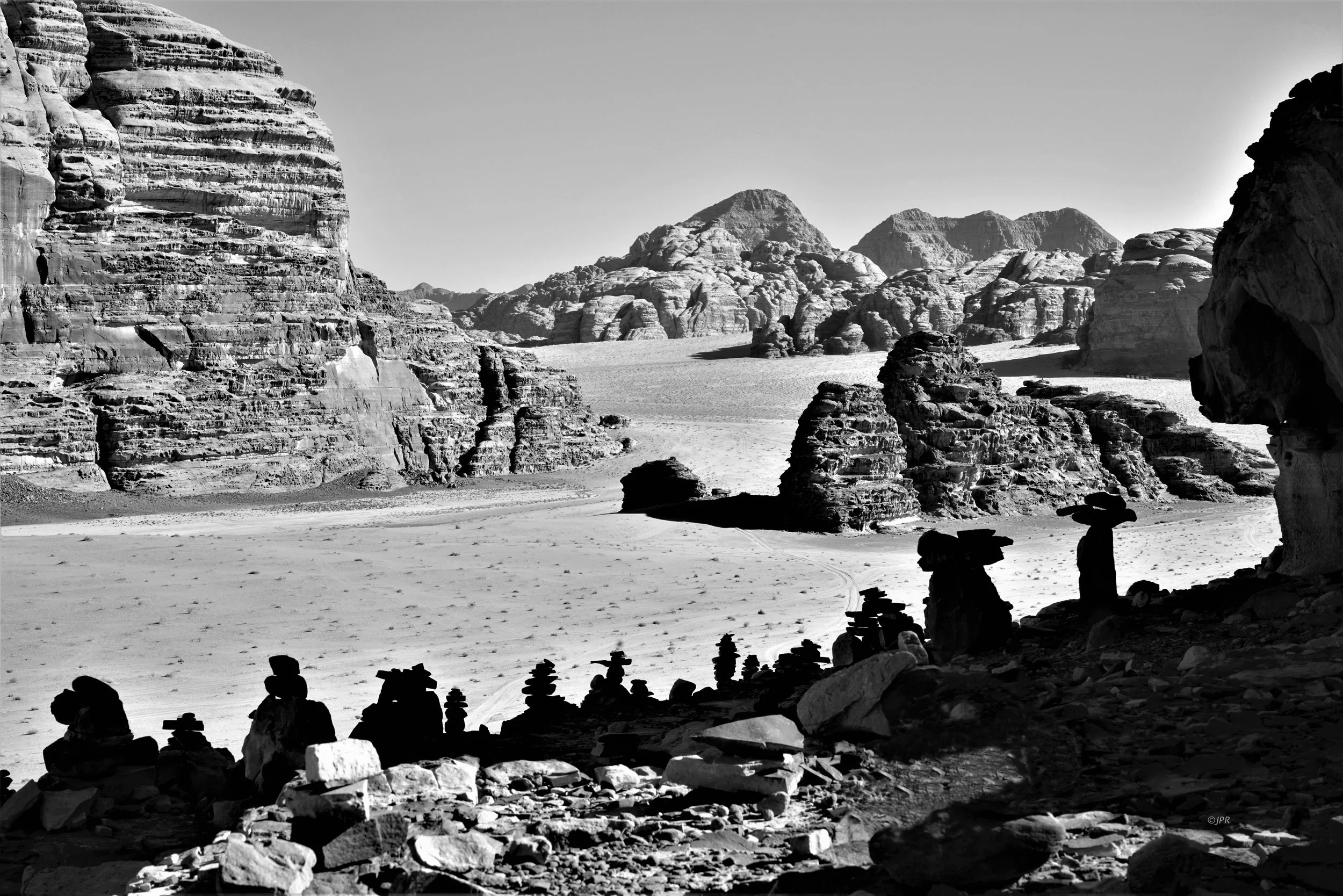 Paysage désertique avec des formations rocheuses impressionnantes, vue depuis une grotte ou un abri naturel, en noir et blanc.