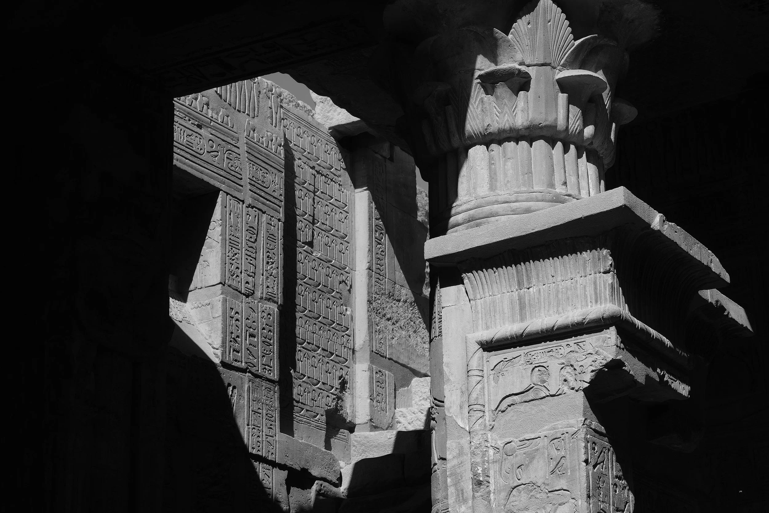 Colonnes et hiéroglyphes antiques en pierre dans un site archéologique égyptien, avec ombres projetées et détails sculptés.